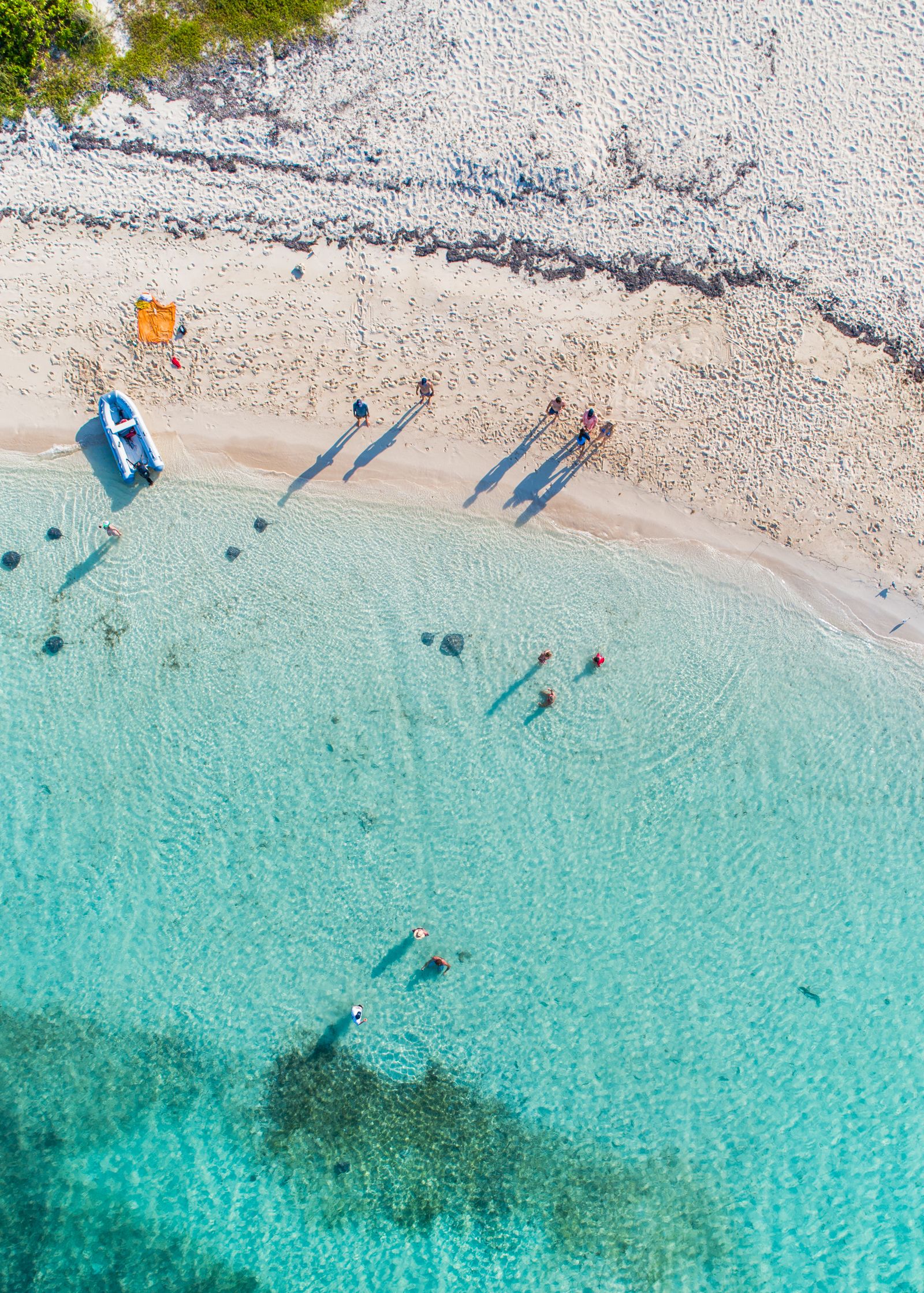 People wading off a white sand beach into clear turquoise water, seen from above