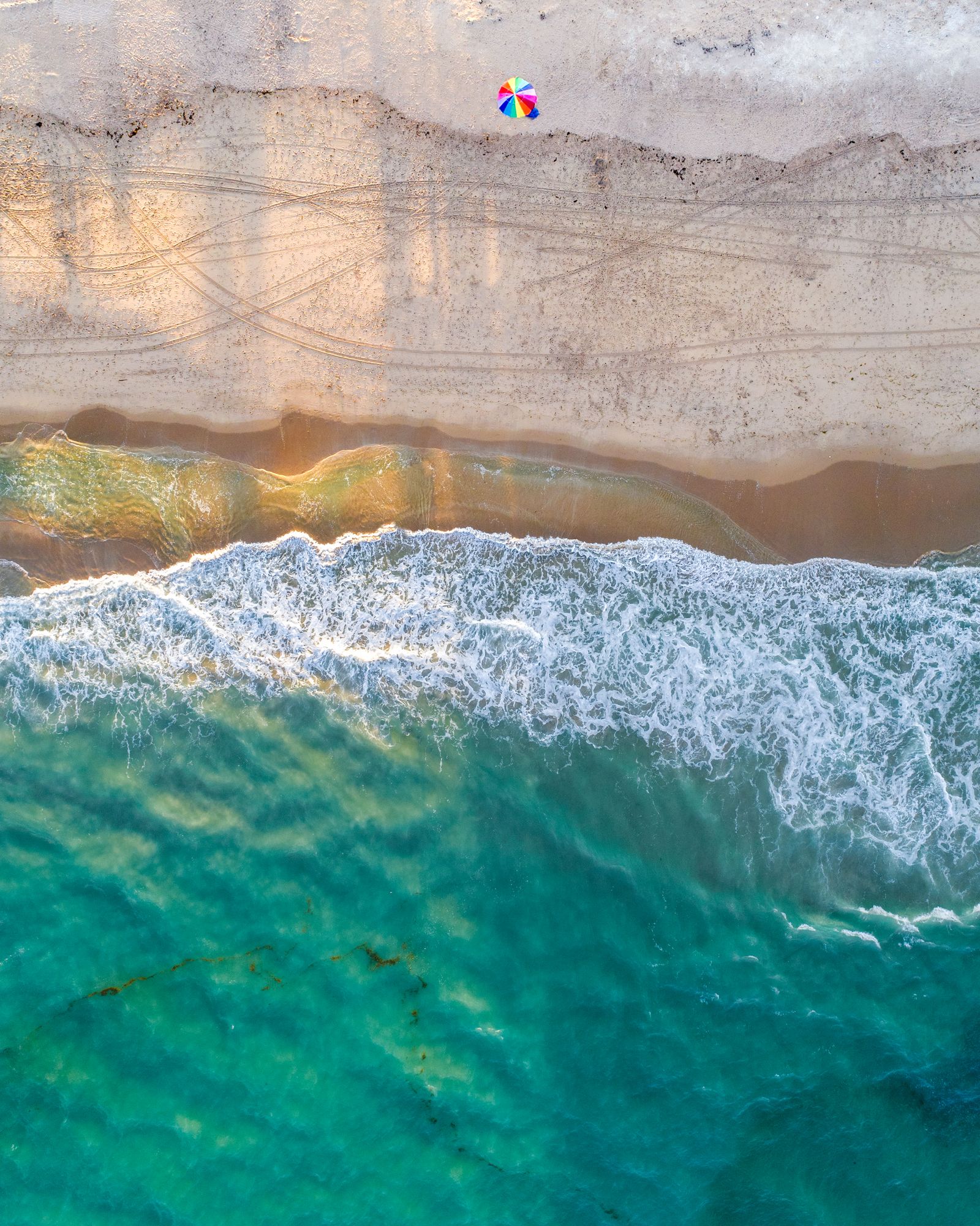 A single beach umbrella on wide sand above a band of breaking waves