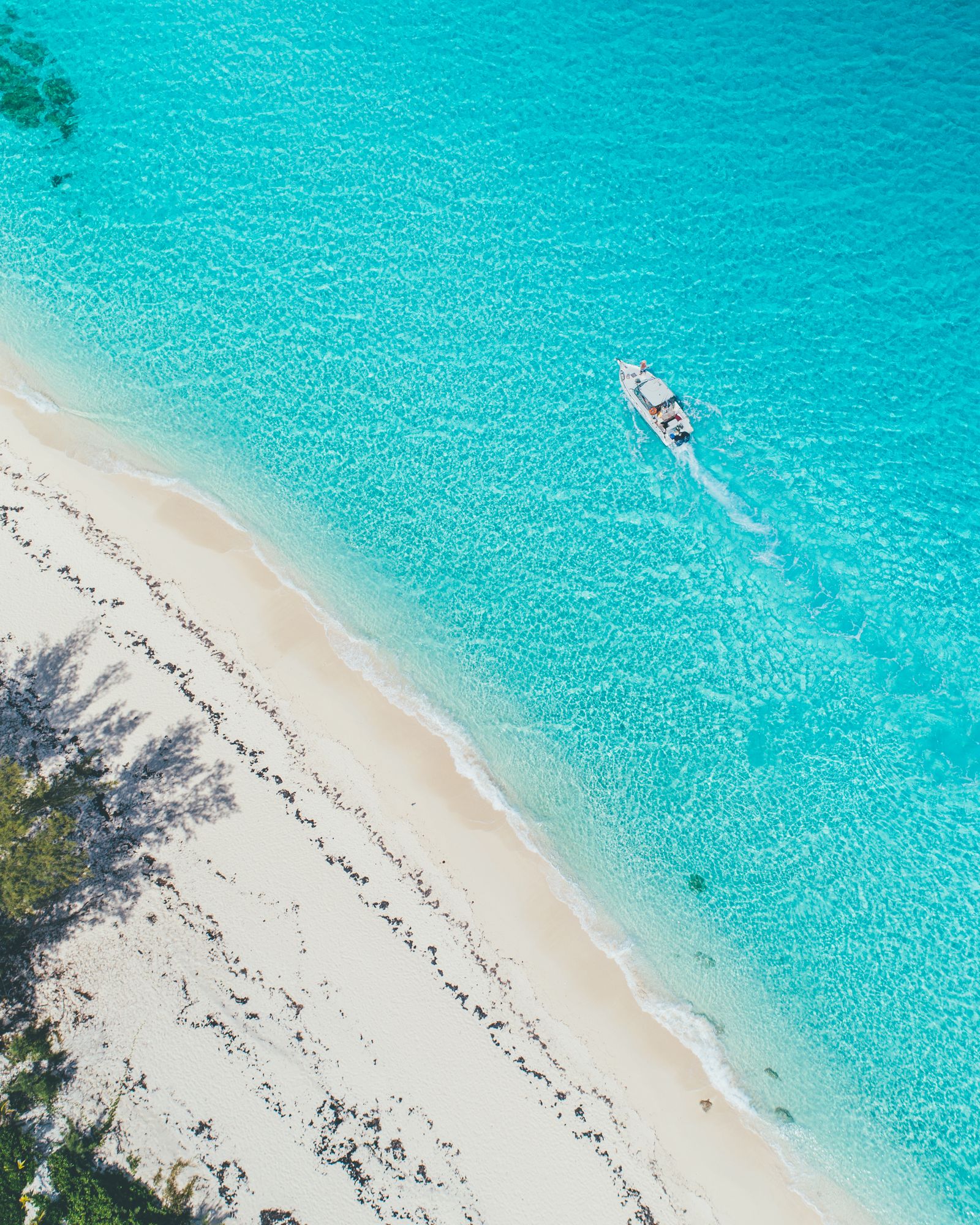 Aerial of a boat running along a white sand shoreline in bright turquoise water in Bimini