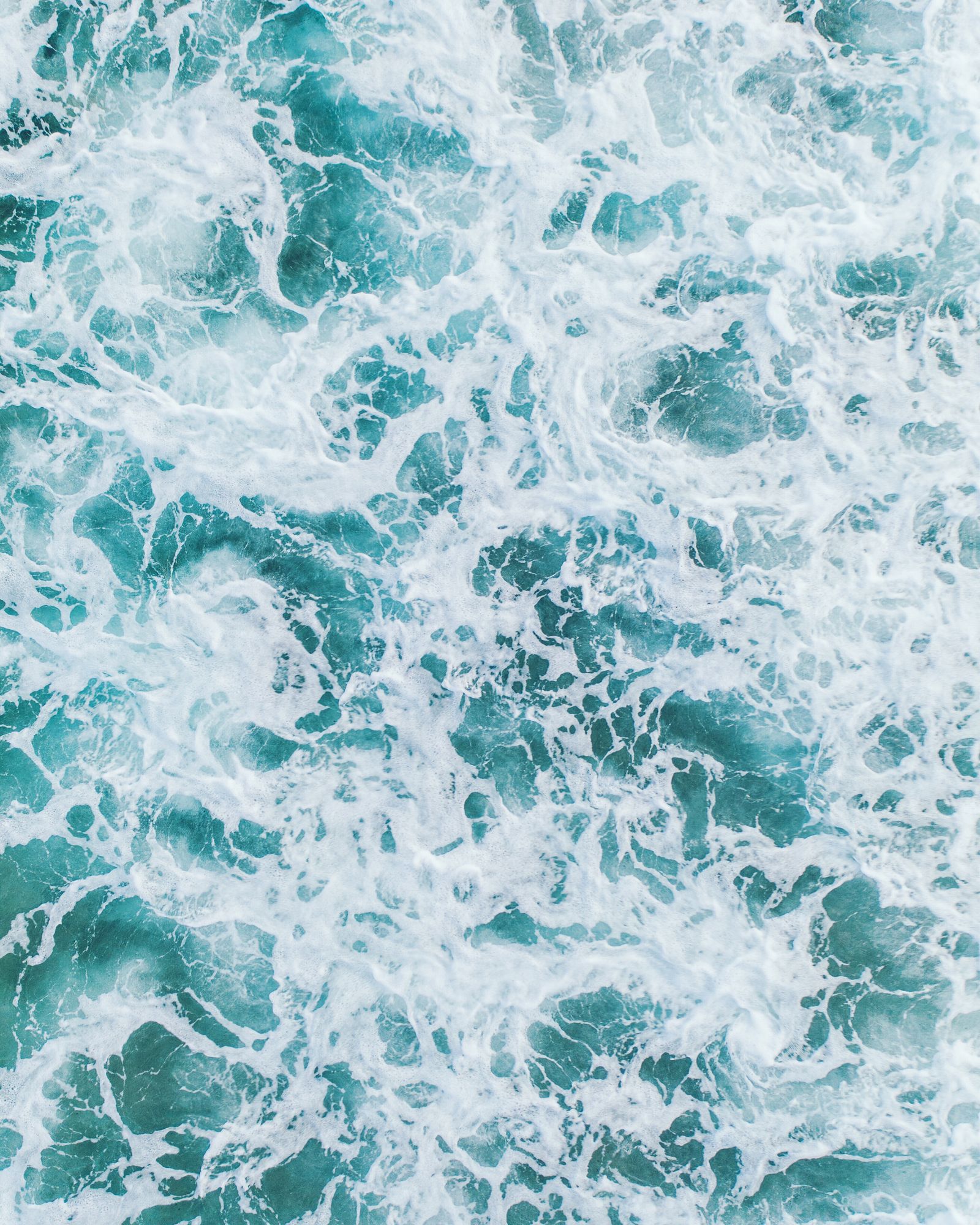 Swirling white foam and dark teal water from directly overhead