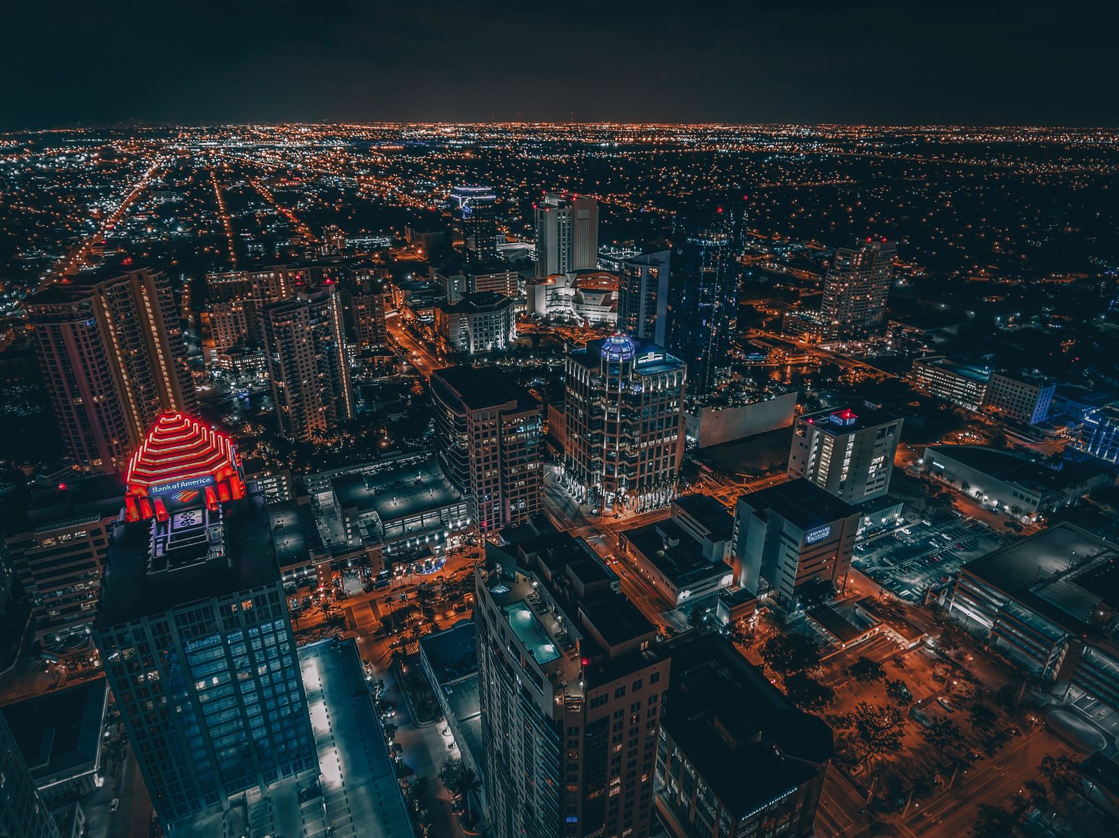 A downtown grid of towers and streets lit orange at night, seen from high above