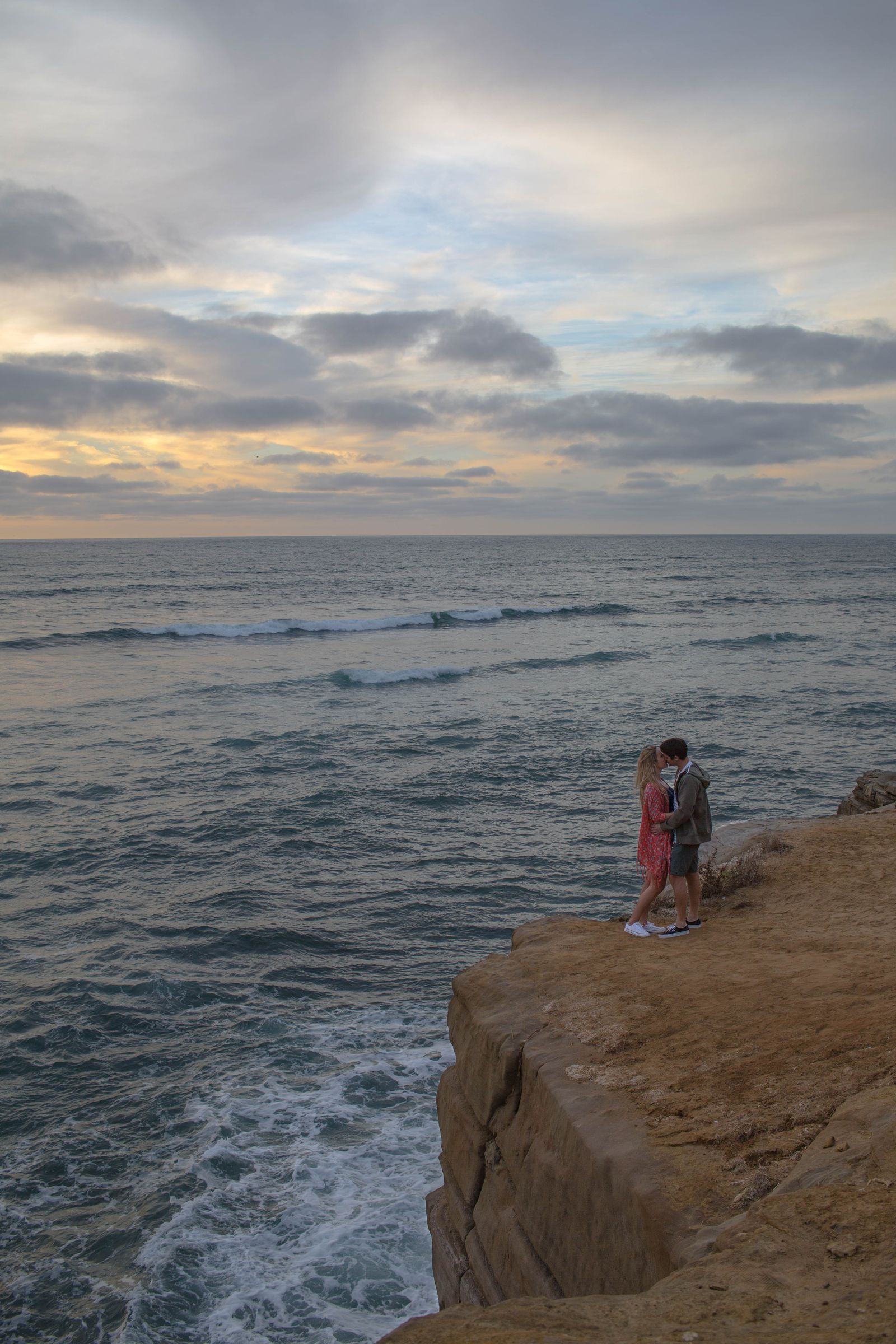 A couple embracing on a sandstone cliff above the ocean at dusk