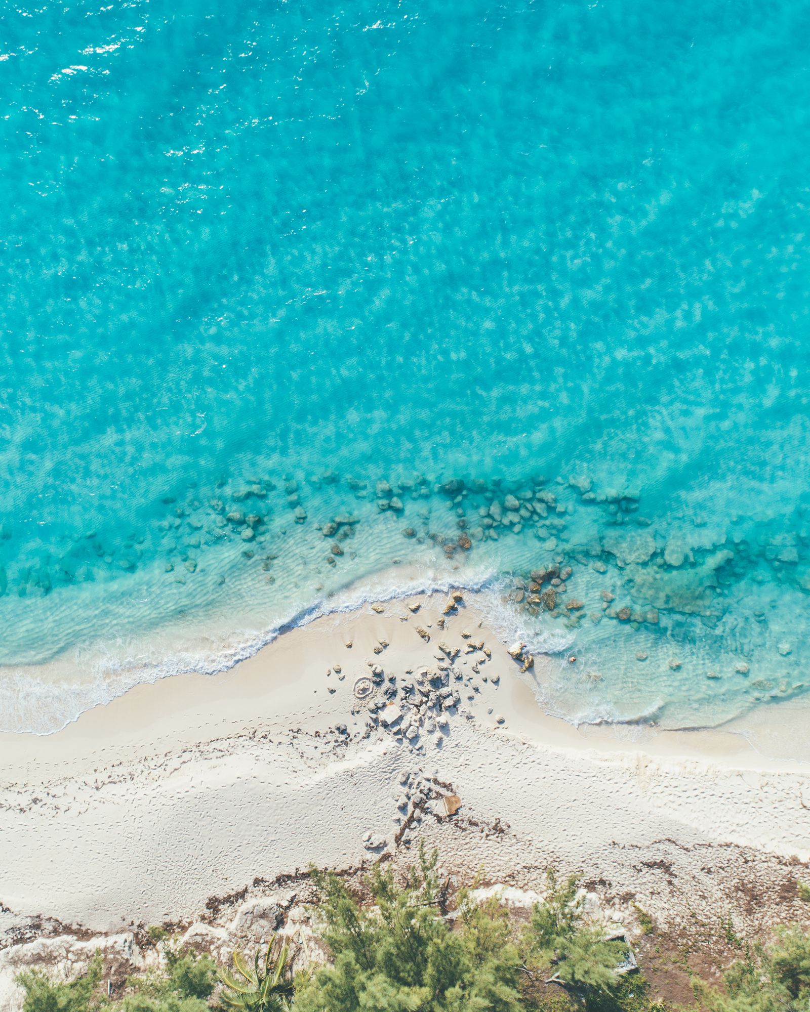 Turquoise water meeting a white sand beach and green dune, seen from above