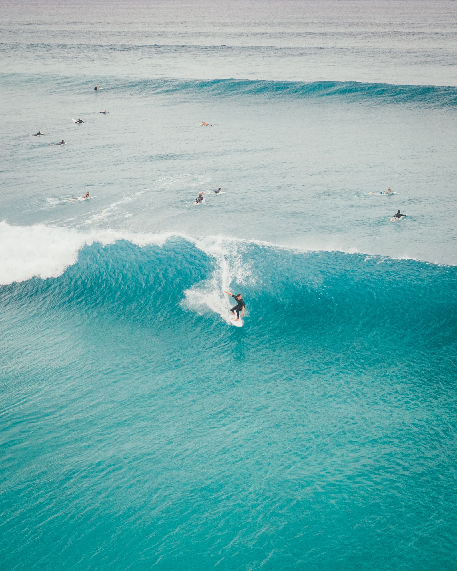 A surfer riding a clean turquoise wave in Delray Beach, others waiting outside