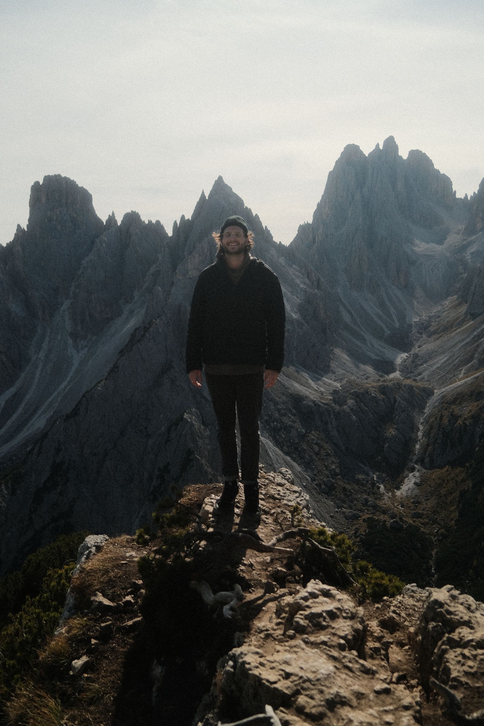 A man standing on a rocky ledge in front of jagged Dolomites peaks