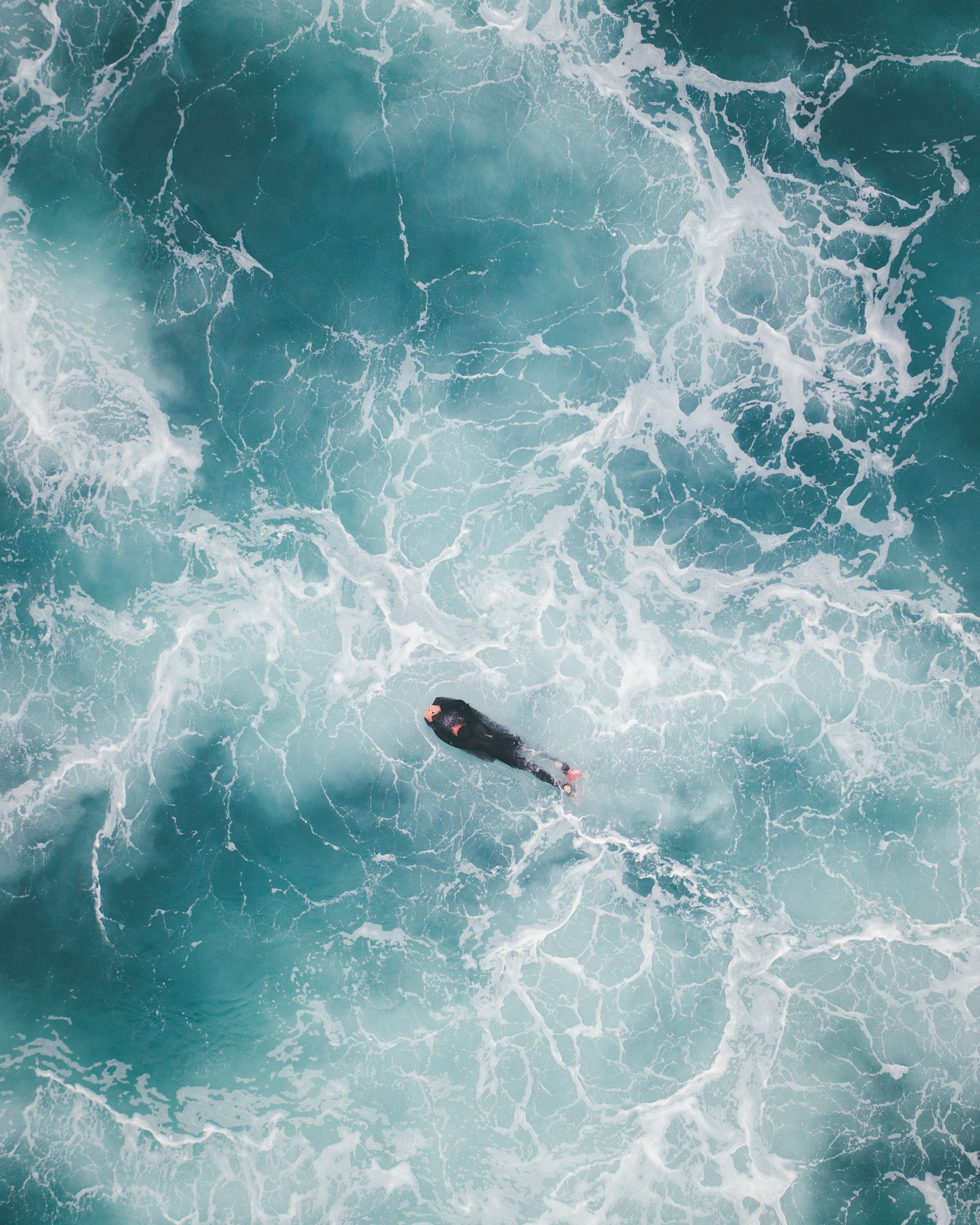 A surfer pushing under foam and turbulent teal water, seen from above
