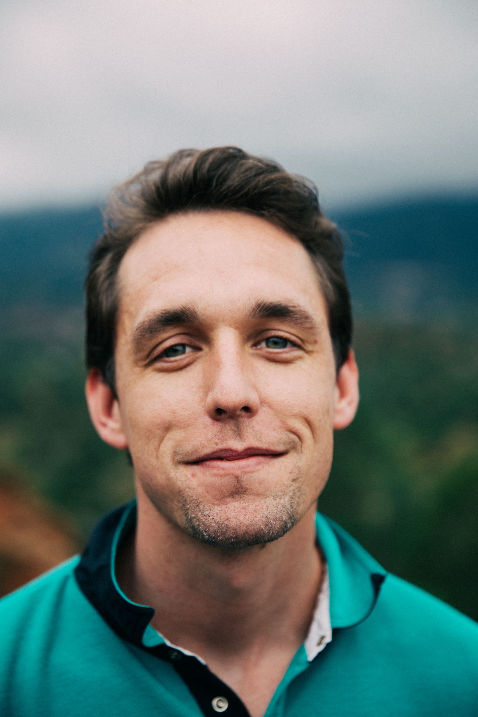 A smiling young man in a teal shirt, close portrait with a soft background