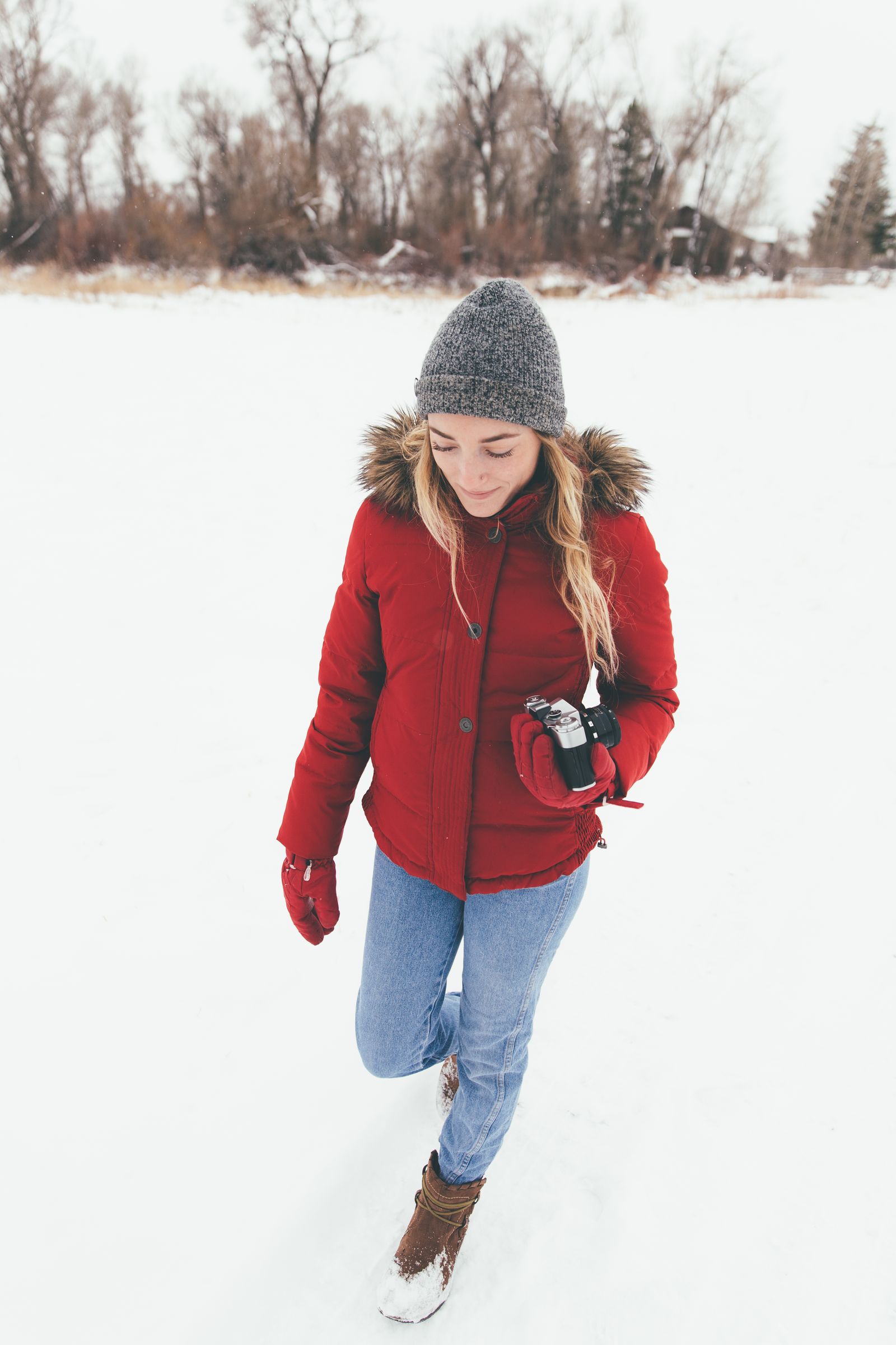 A woman in a red parka holding a camera in a snowy field