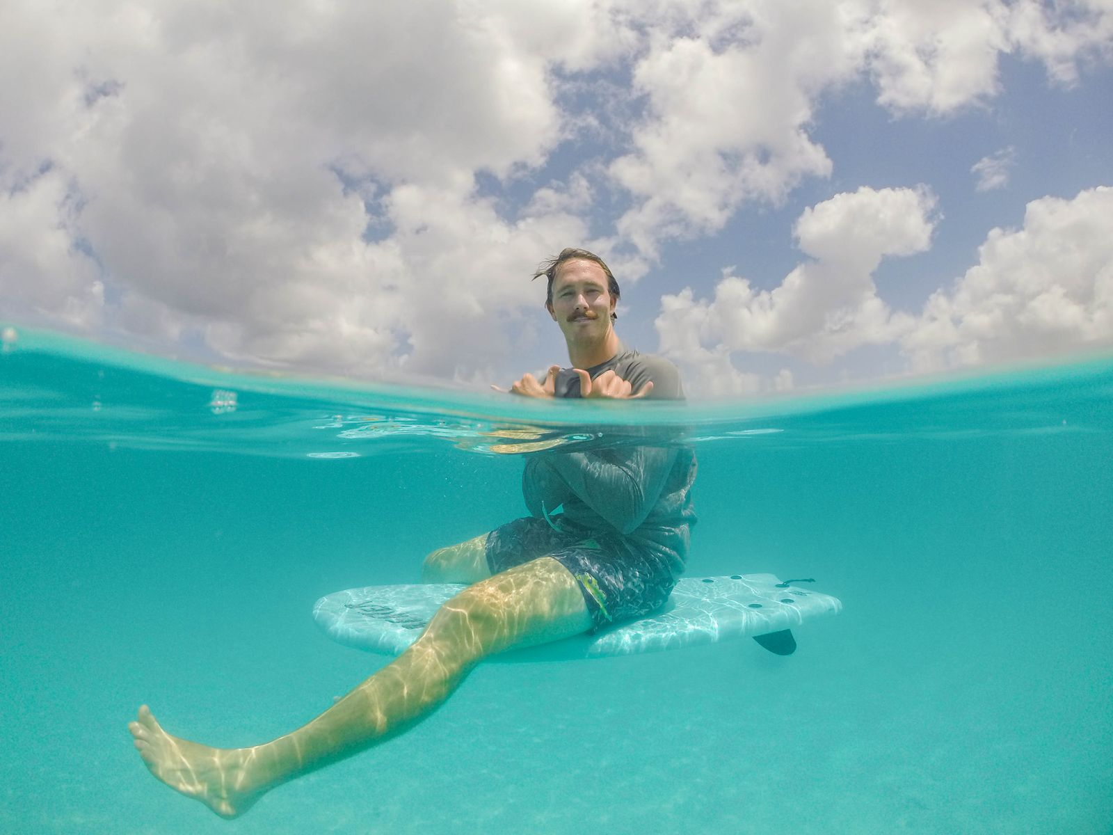 A man sitting on a surfboard half above and half below the waterline in clear water