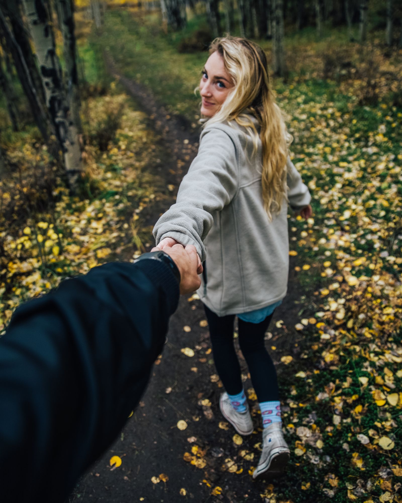 A woman leading the photographer by the hand down a leafy forest path