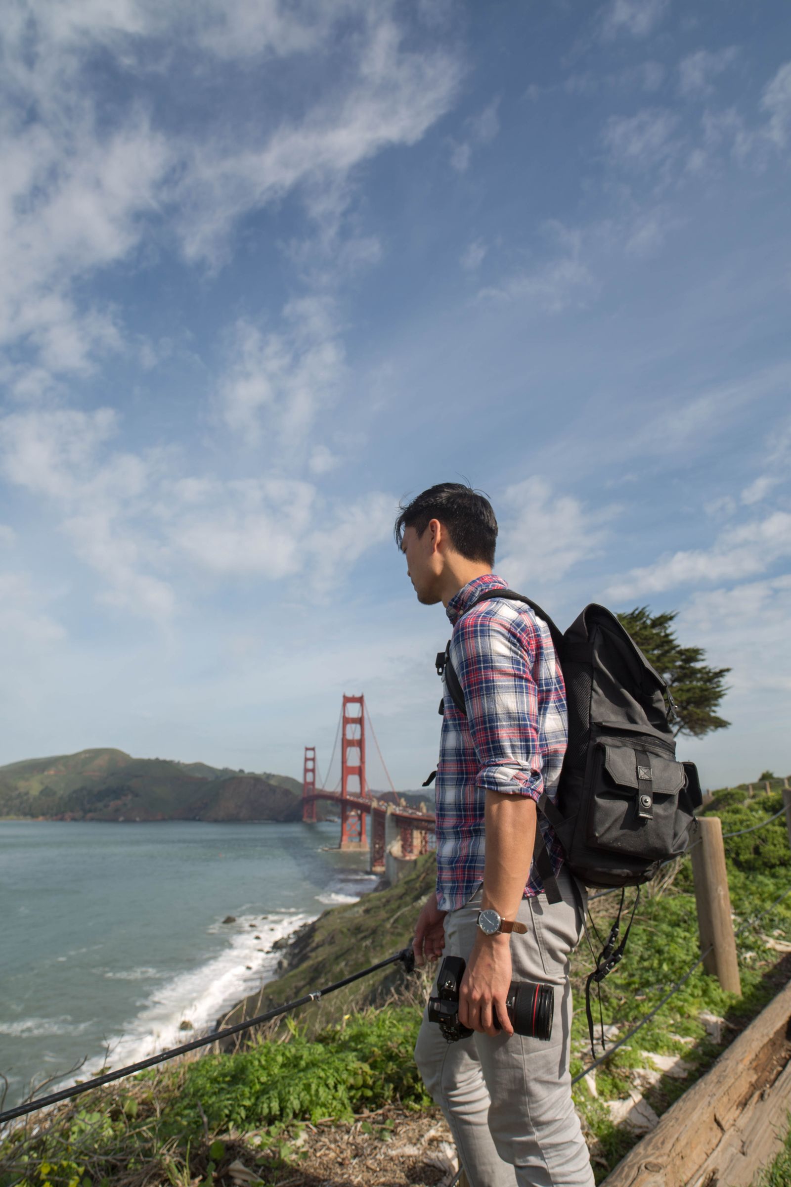 A hiker with a backpack looking out at the Golden Gate Bridge from the coastal cliffs
