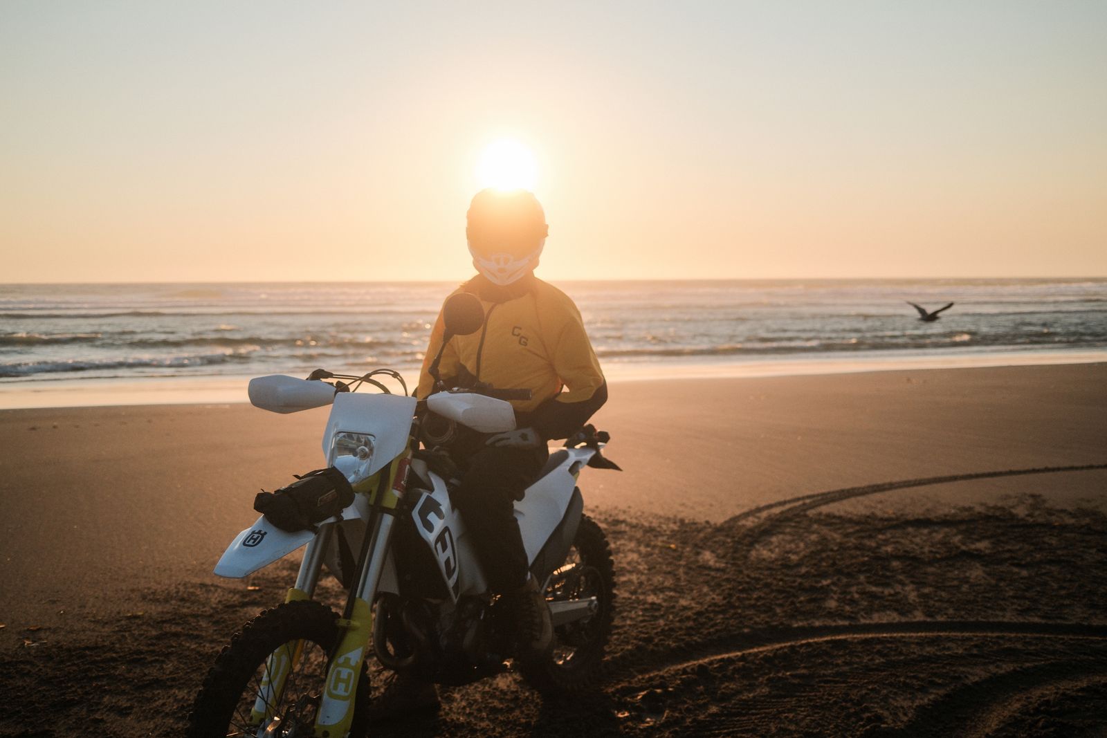 A rider on a dirt bike with the setting sun just above his helmet on an Oregon beach