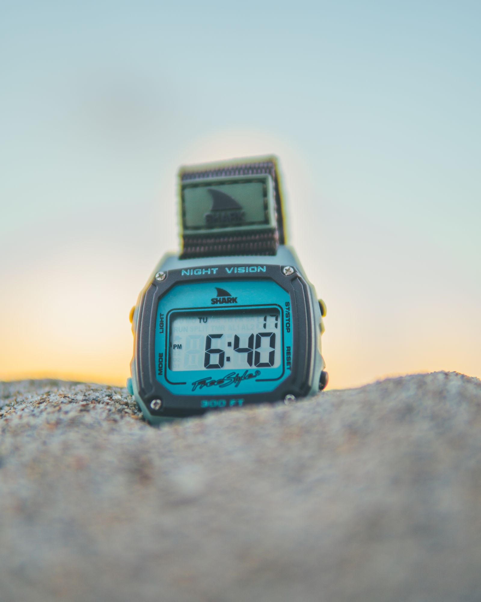 A Freestyle Shark watch propped on a rock at the beach at sunset