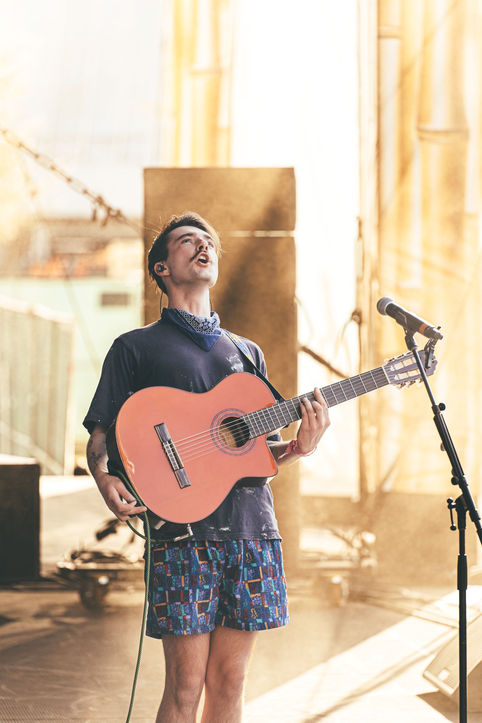 Goth Babe singing with a pink acoustic guitar on a sunlit outdoor stage