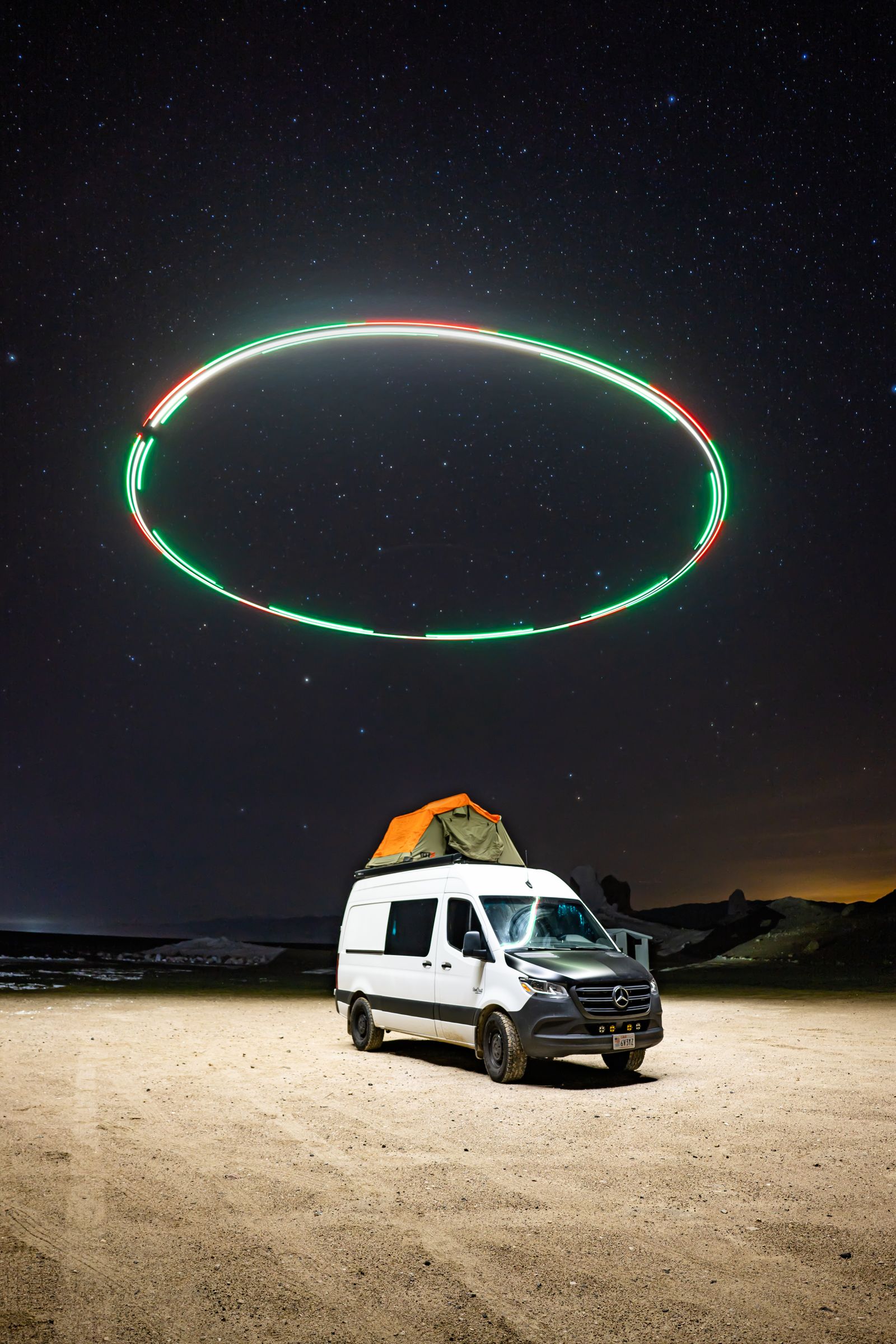 A glowing ring of light hovering in a starry sky above a camper van on the desert floor