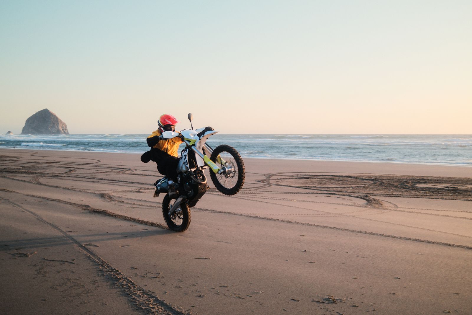 A rider pulling a wheelie on the sand, Haystack Rock and the ocean behind