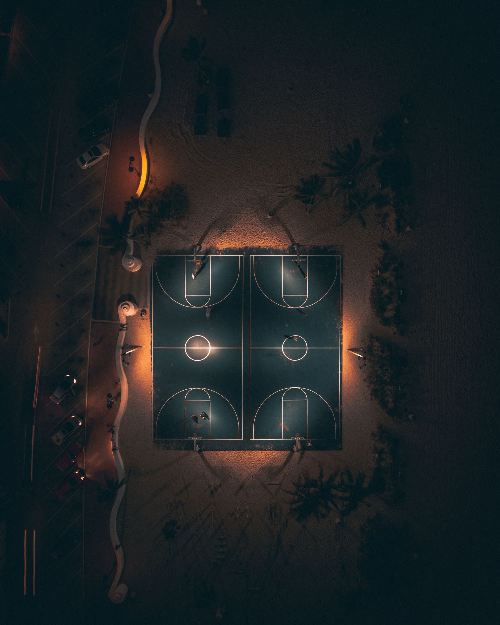 Lit basketball courts glowing at night in Fort Lauderdale, surrounded by dark trees, from directly above