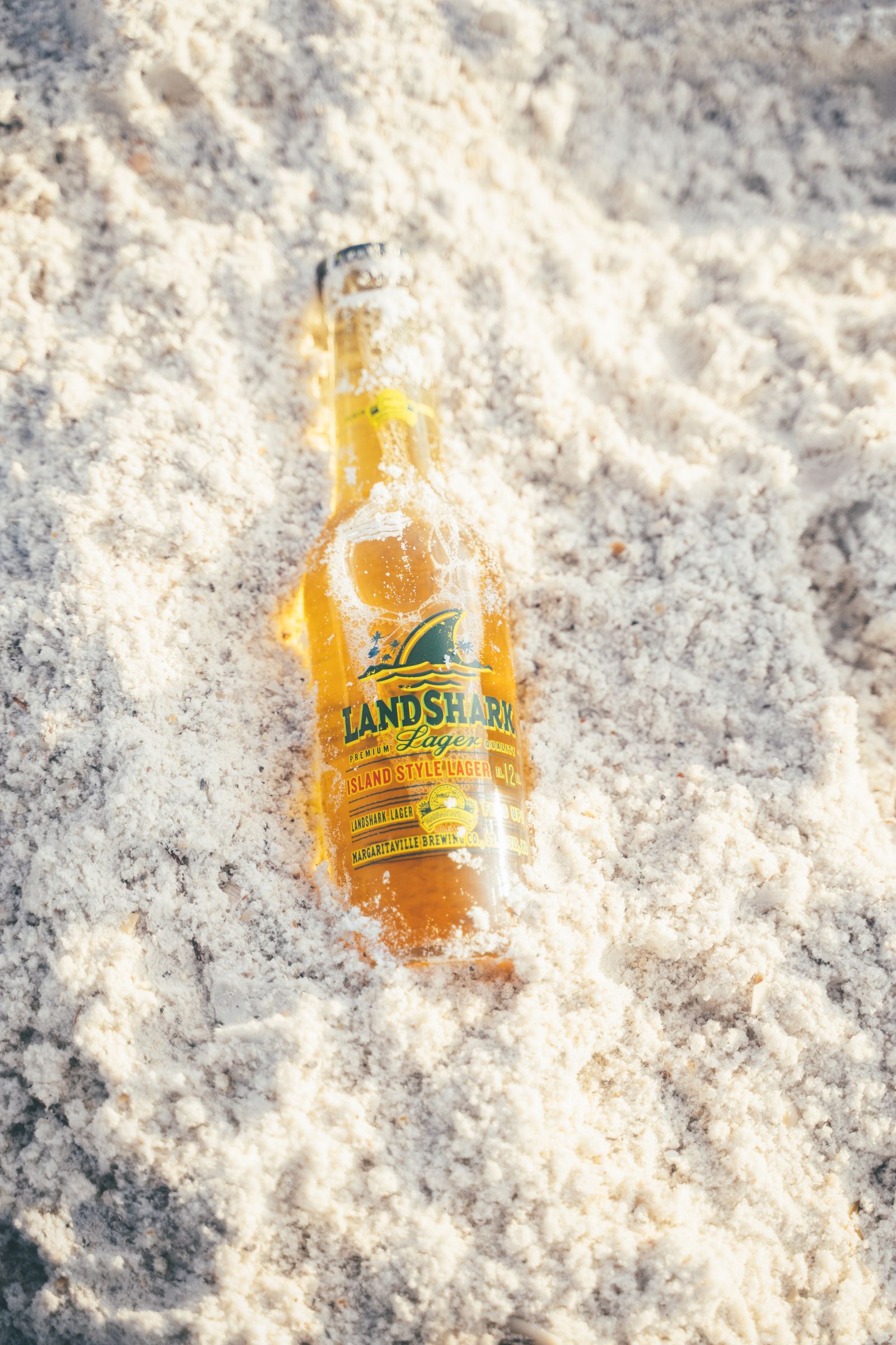 A bottle of Landshark lager lying in fine white sand