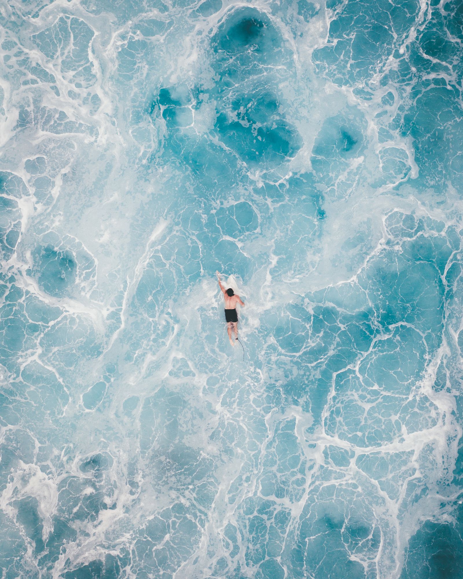 A surfer floating in swirling white water and foam, seen from straight above