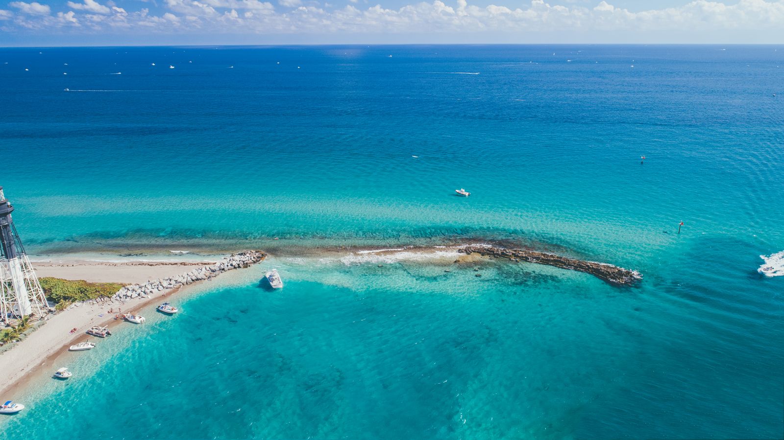 A long jetty and inlet with boats heading out into bright blue water