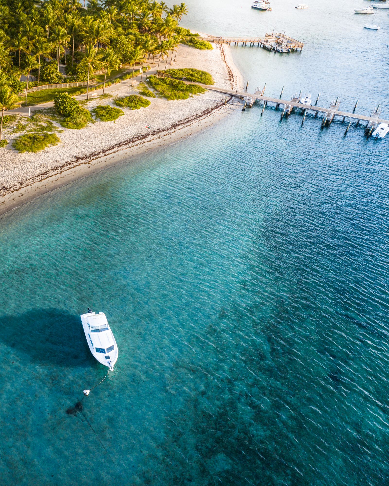 Aerial of a long dock off a palm-lined beach with a boat anchored in clear blue water near Jupiter