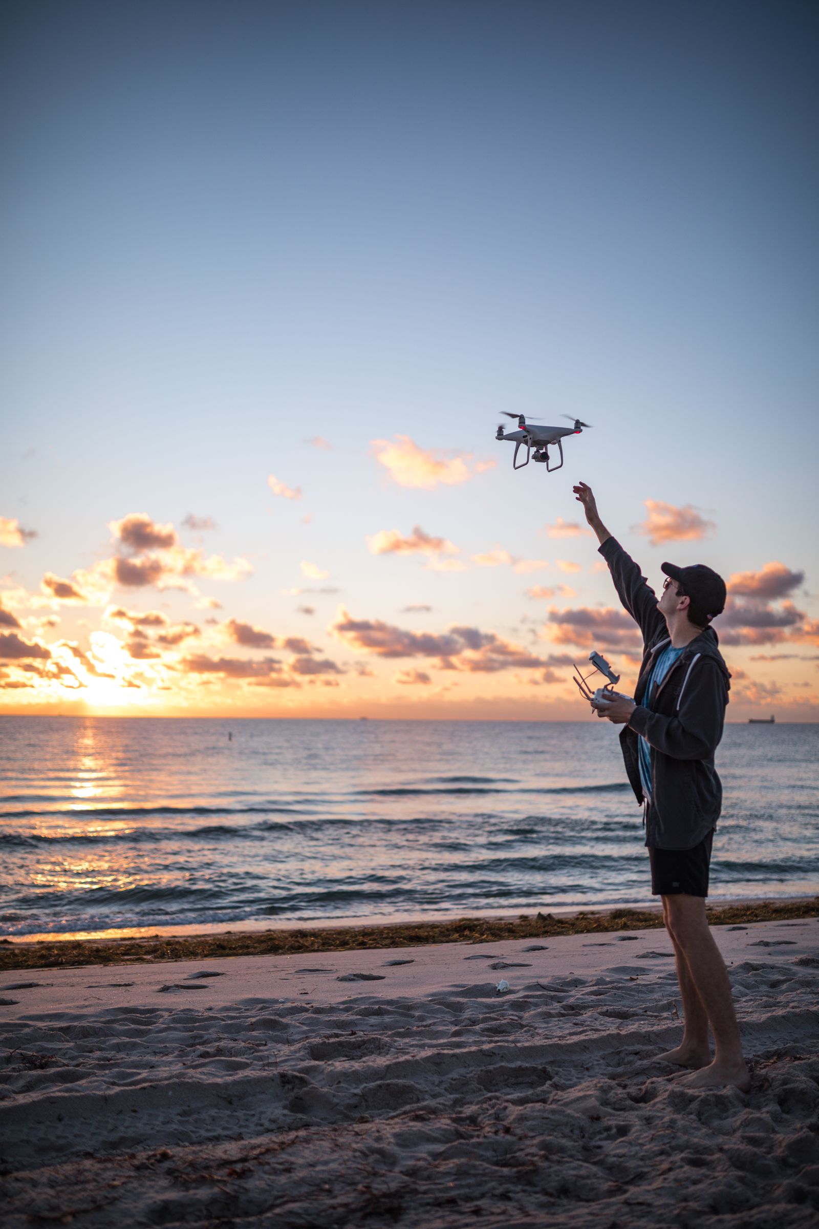 A drone pilot hand-launching a DJI Phantom over the beach at sunrise