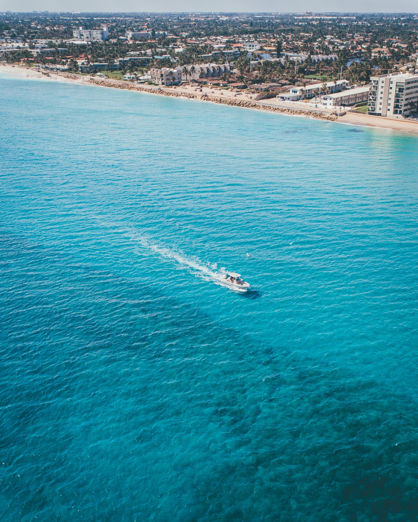 A single boat carving a white wake across deep blue water off a South Florida beach