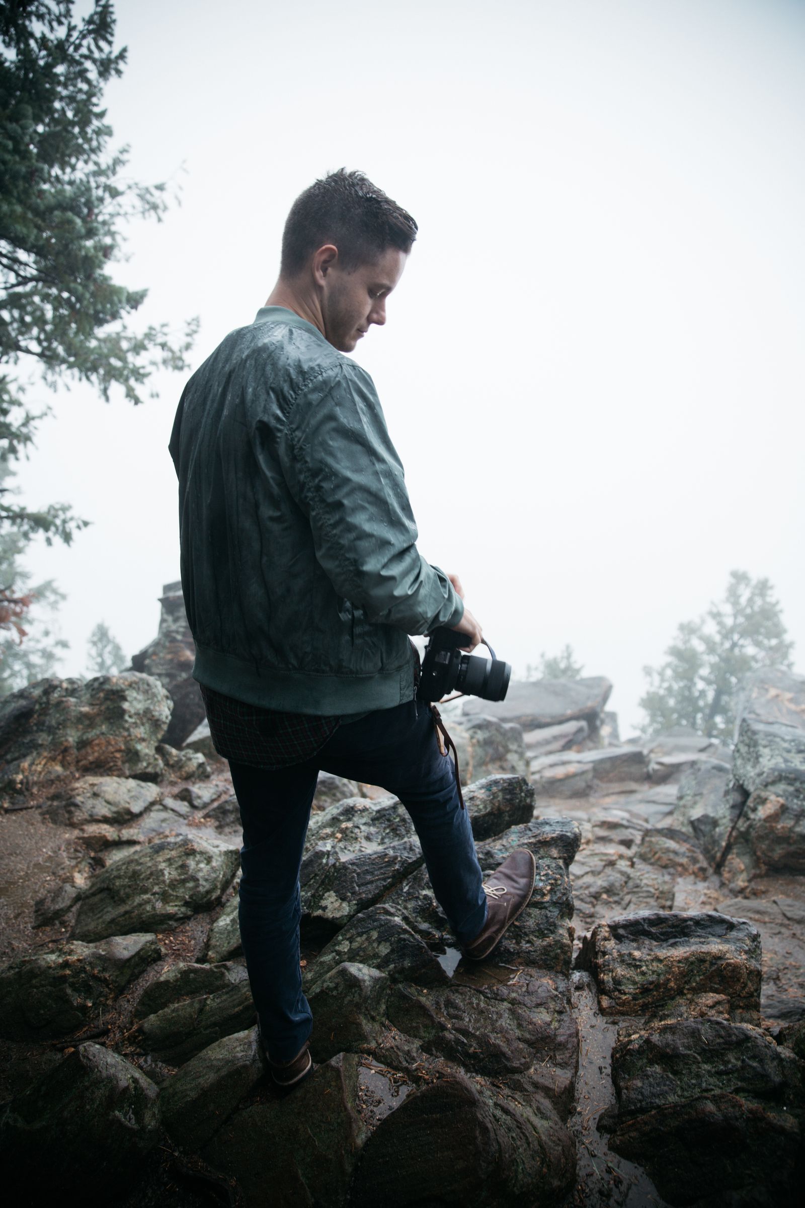 A photographer standing on a rocky outcrop in the fog, camera in hand