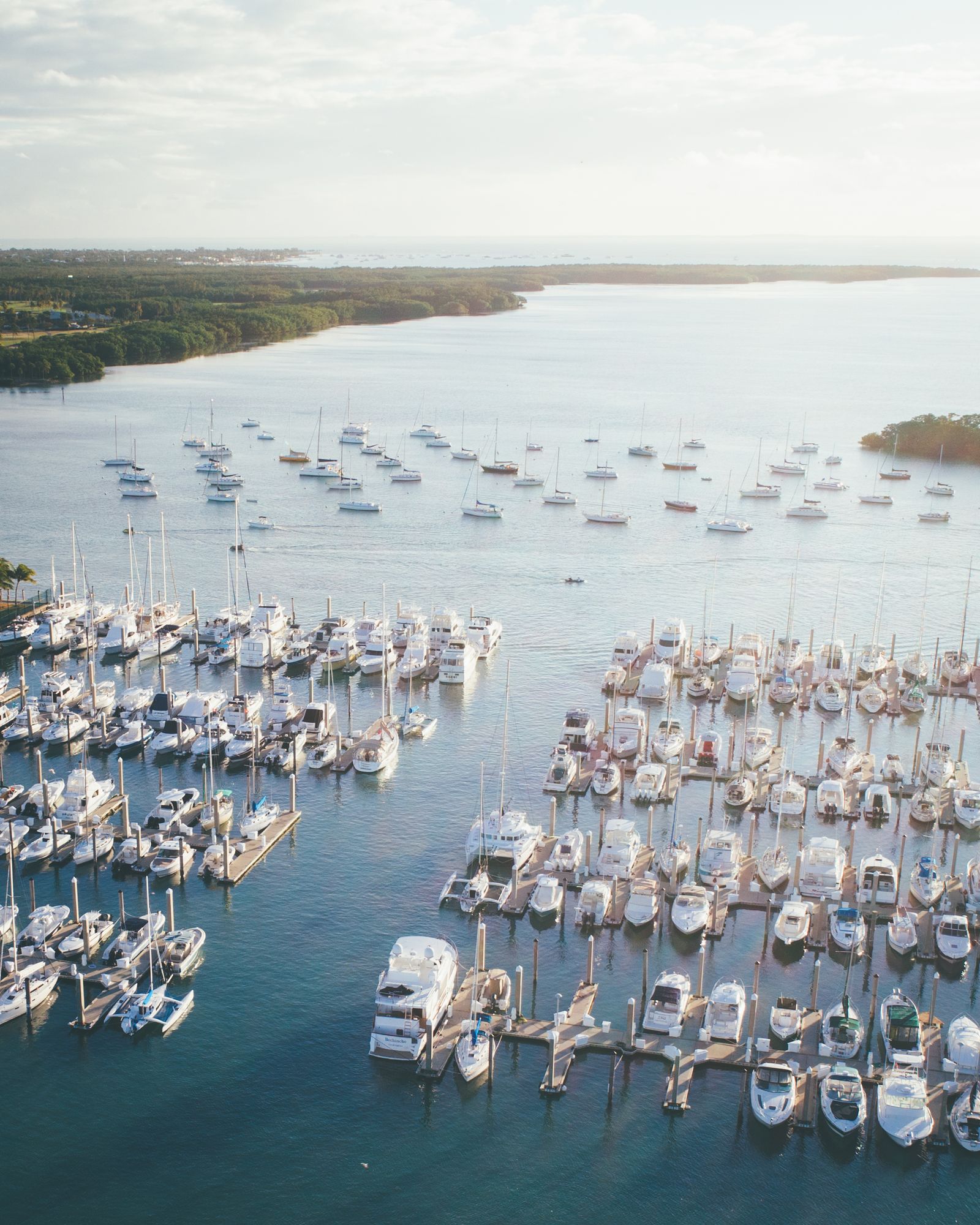 A marina packed with sailboats and powerboats on calm blue water, seen from the air