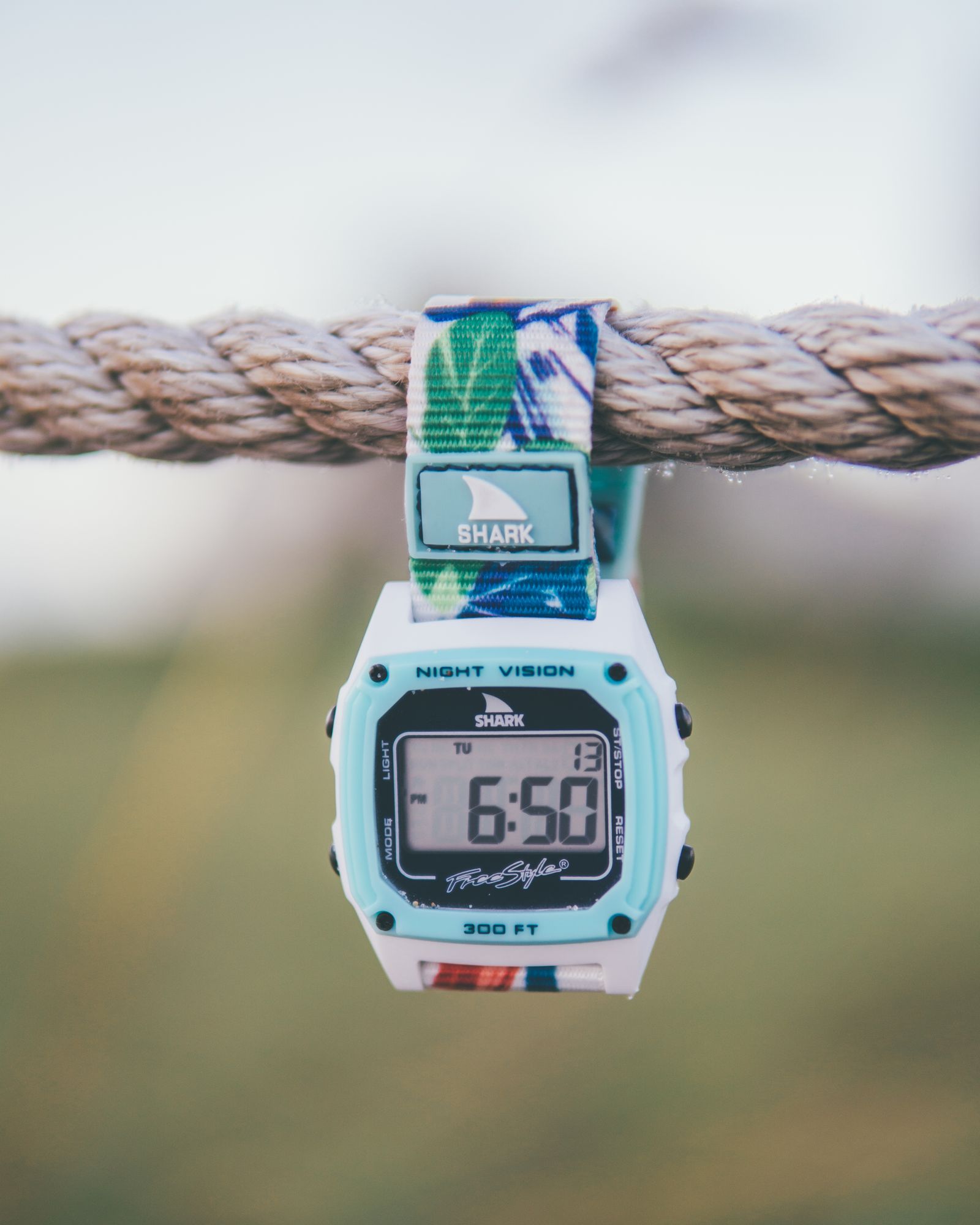 A Freestyle Shark watch hanging from a rope, its screen lit up