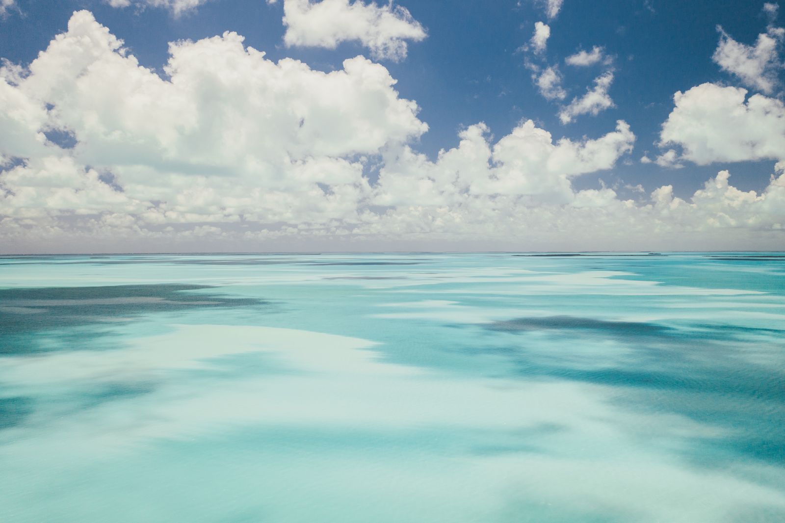 Bright cumulus clouds over a band of glowing turquoise water