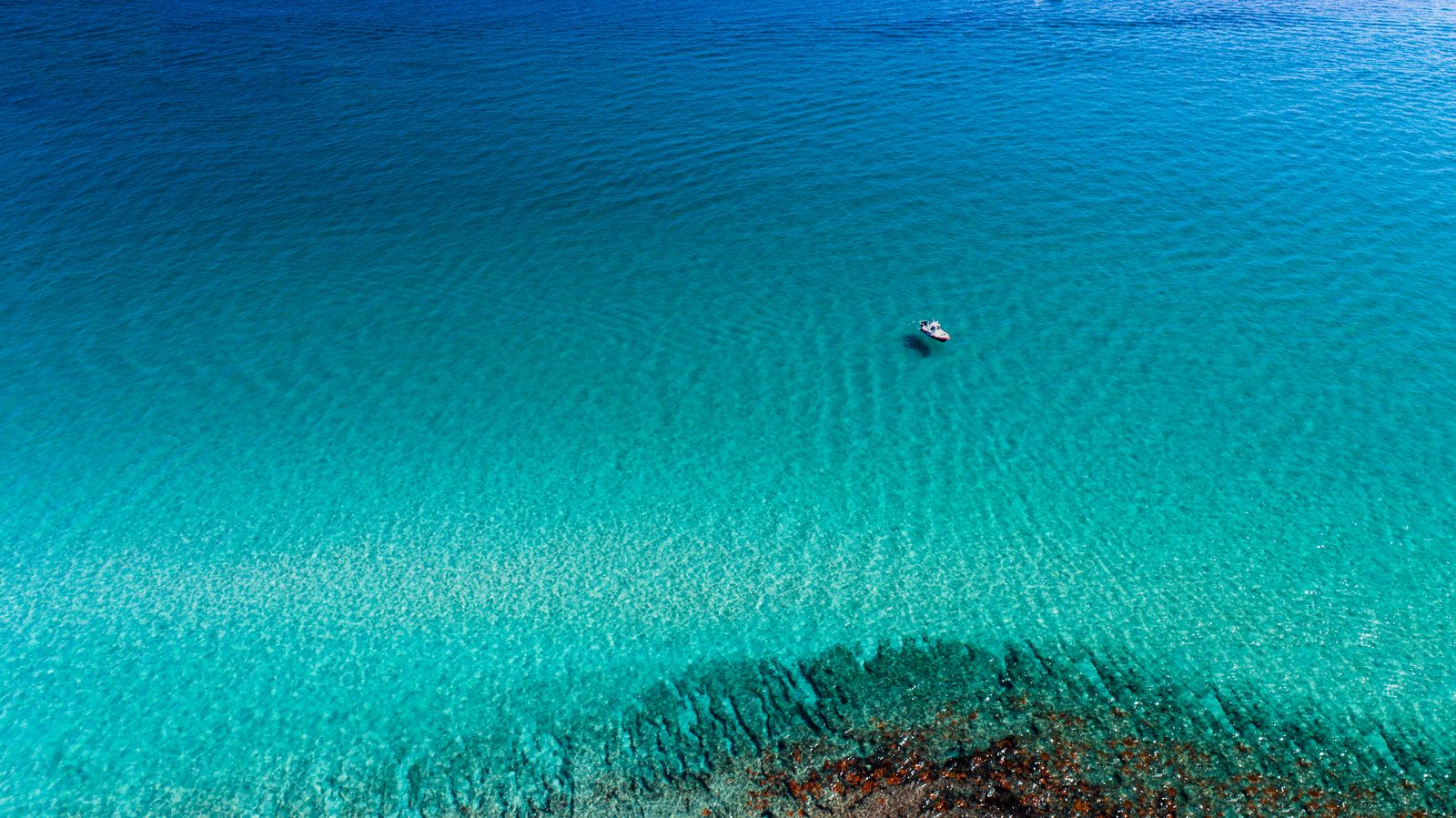 A small boat alone on a wide sheet of blue water over a shallow reef
