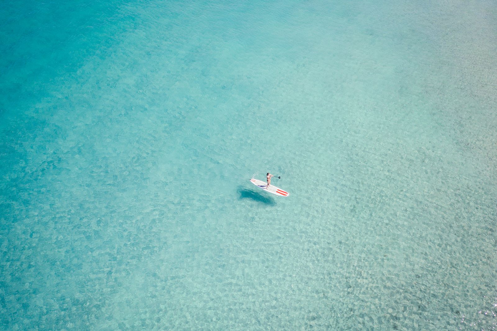 A lone paddleboarder on vast pale turquoise water