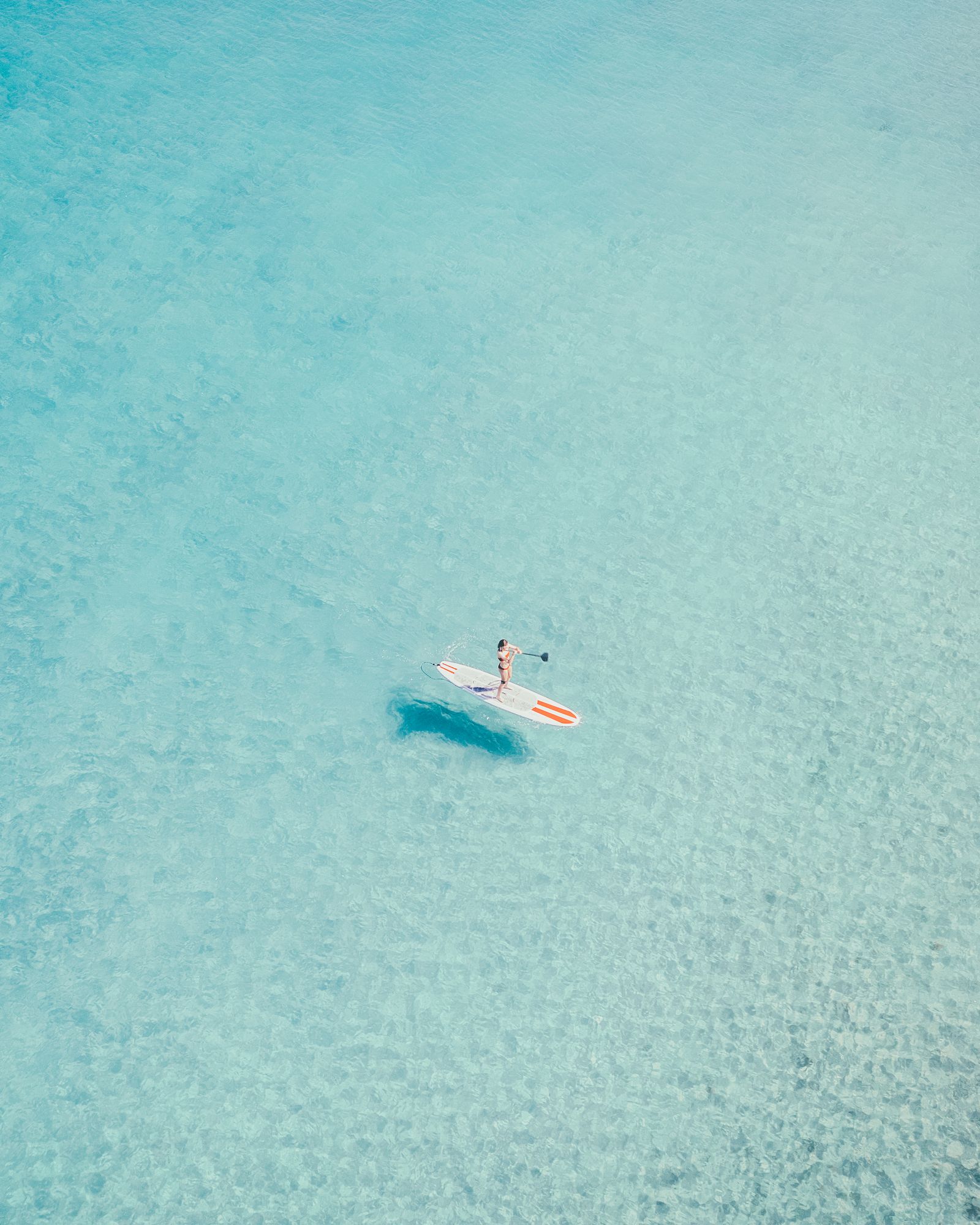 A paddleboarder and their shadow on clear turquoise water off Deerfield Beach