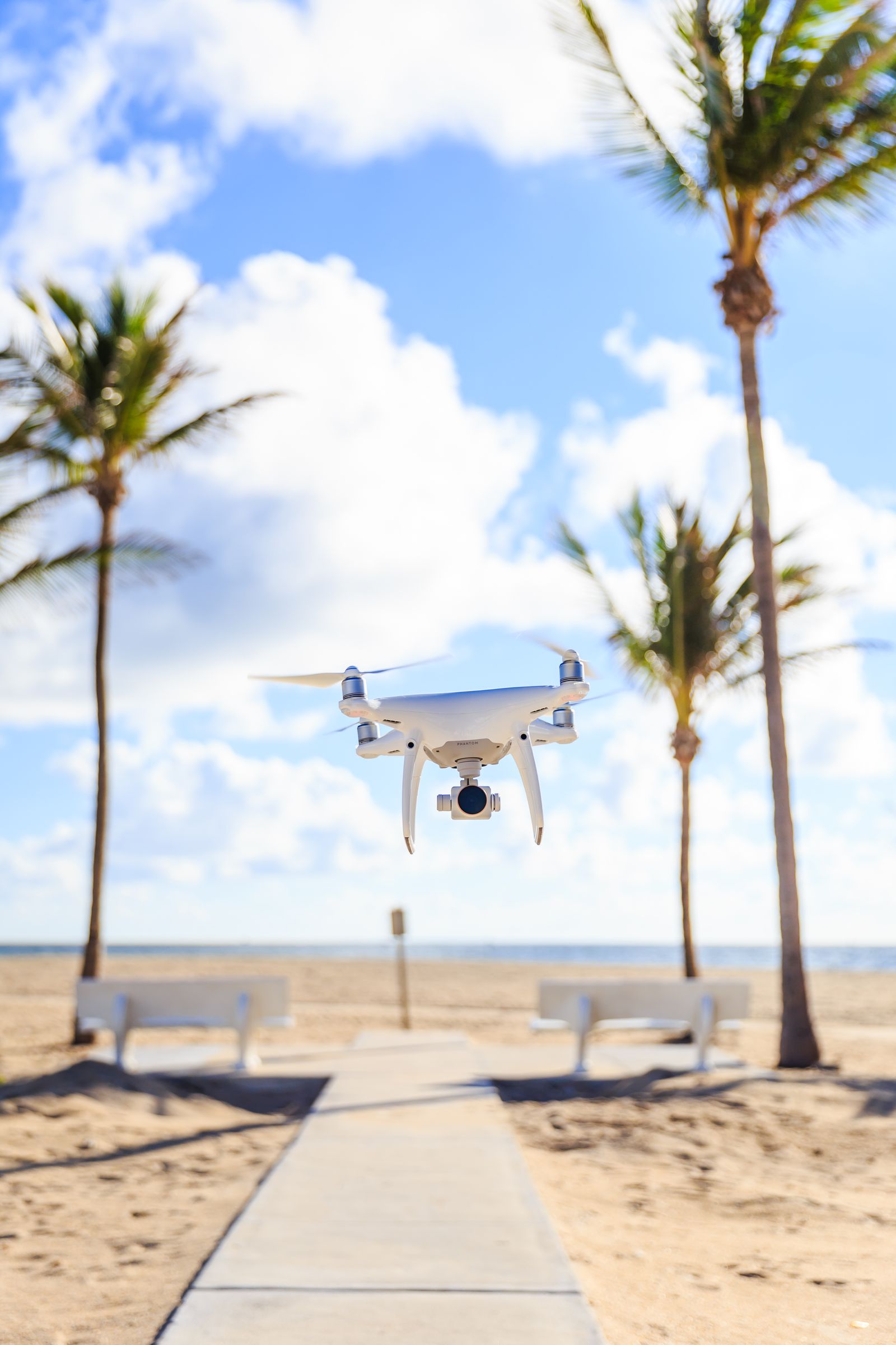 A DJI Phantom hovering above a beach boardwalk between palm trees