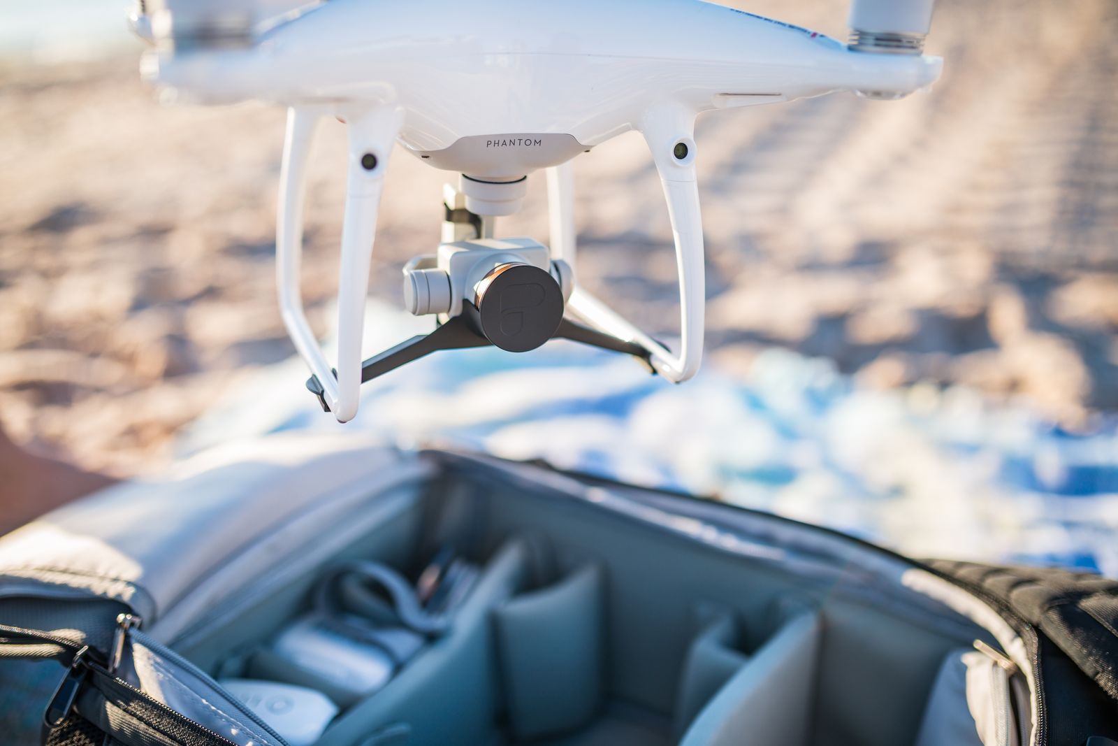 A DJI Phantom 4 Pro fitted with PolarPro filters hovering over an open camera bag on the beach