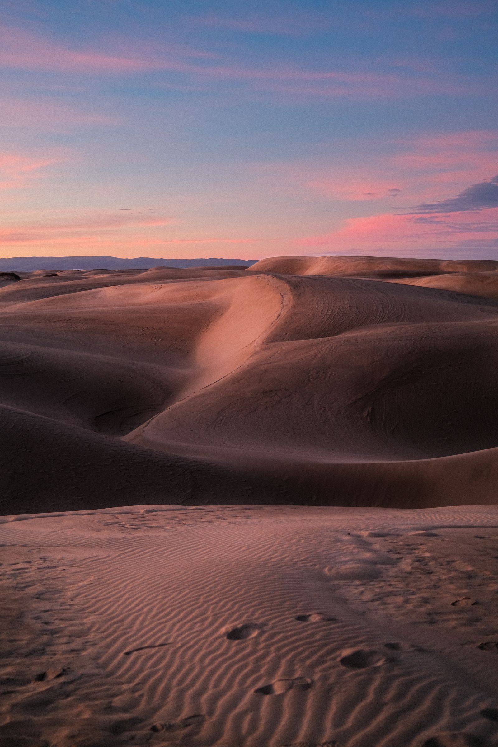 Rolling sand dunes under a pink and purple sunset sky