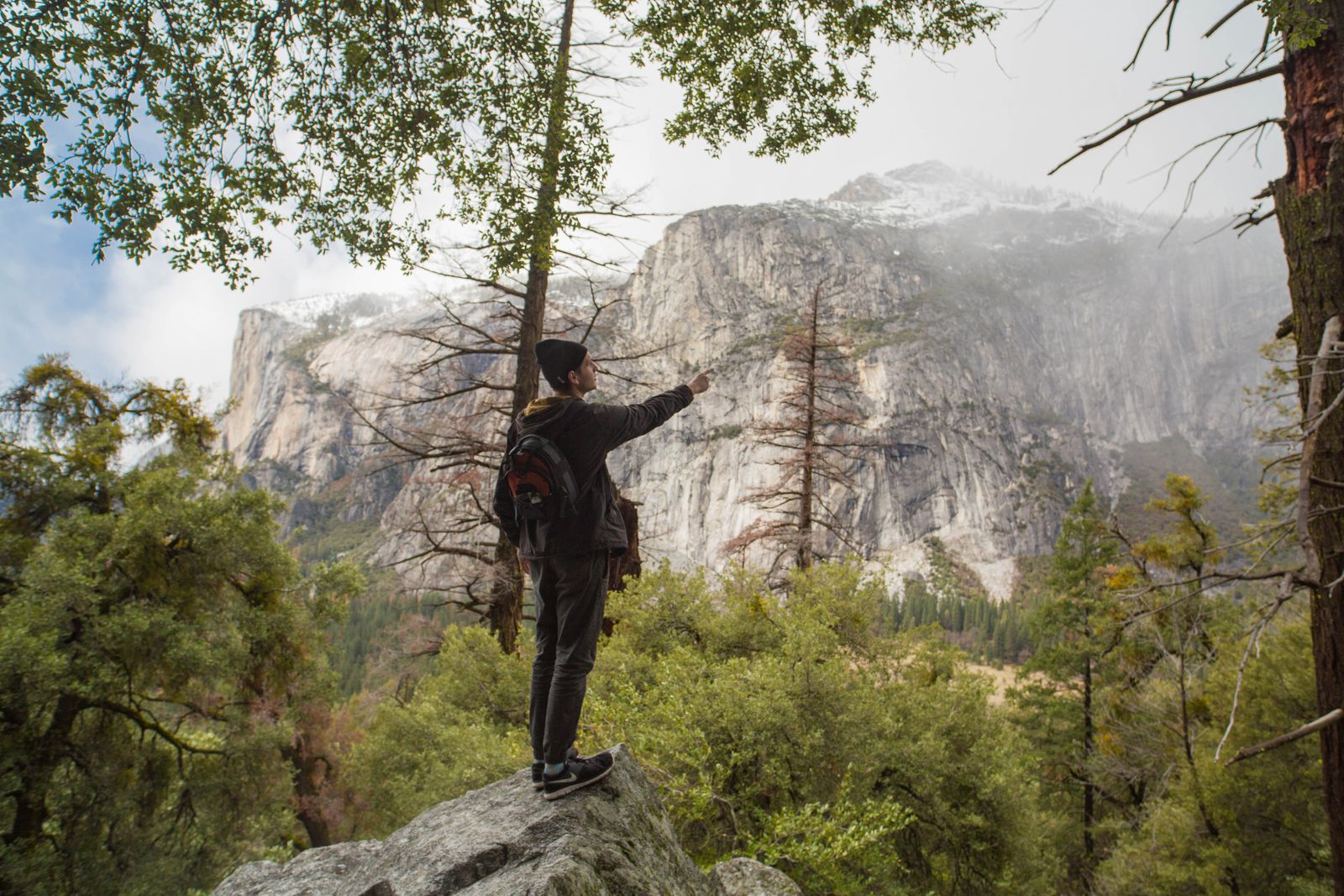 A hiker pointing across Yosemite Valley toward its granite walls