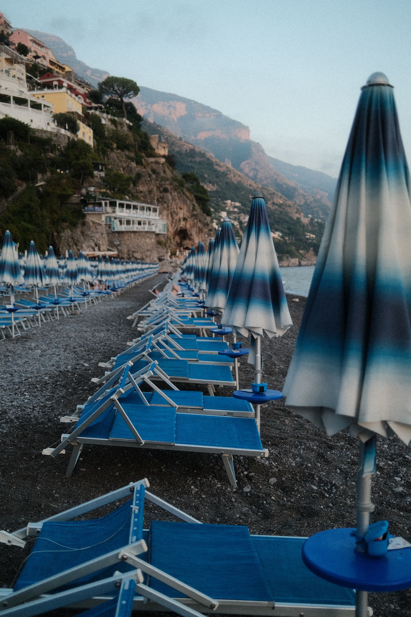 Rows of blue striped umbrellas and loungers on a pebble beach in Positano