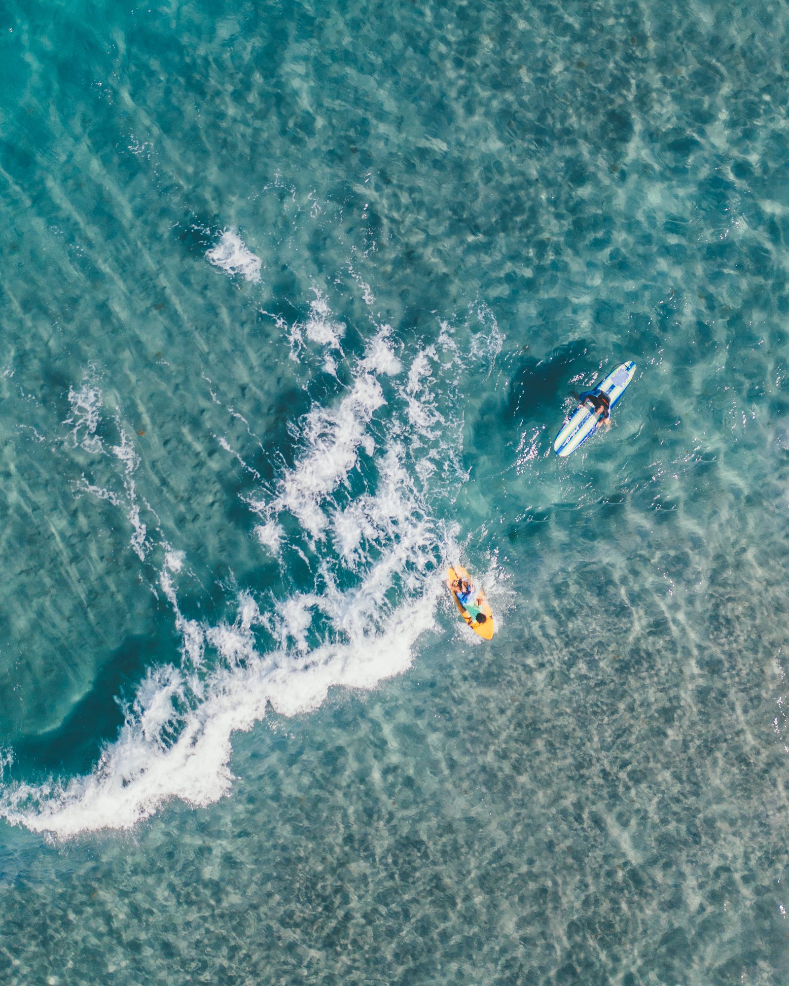 Surfers paddling out through a breaking wave at Red Reef Beach, seen from above