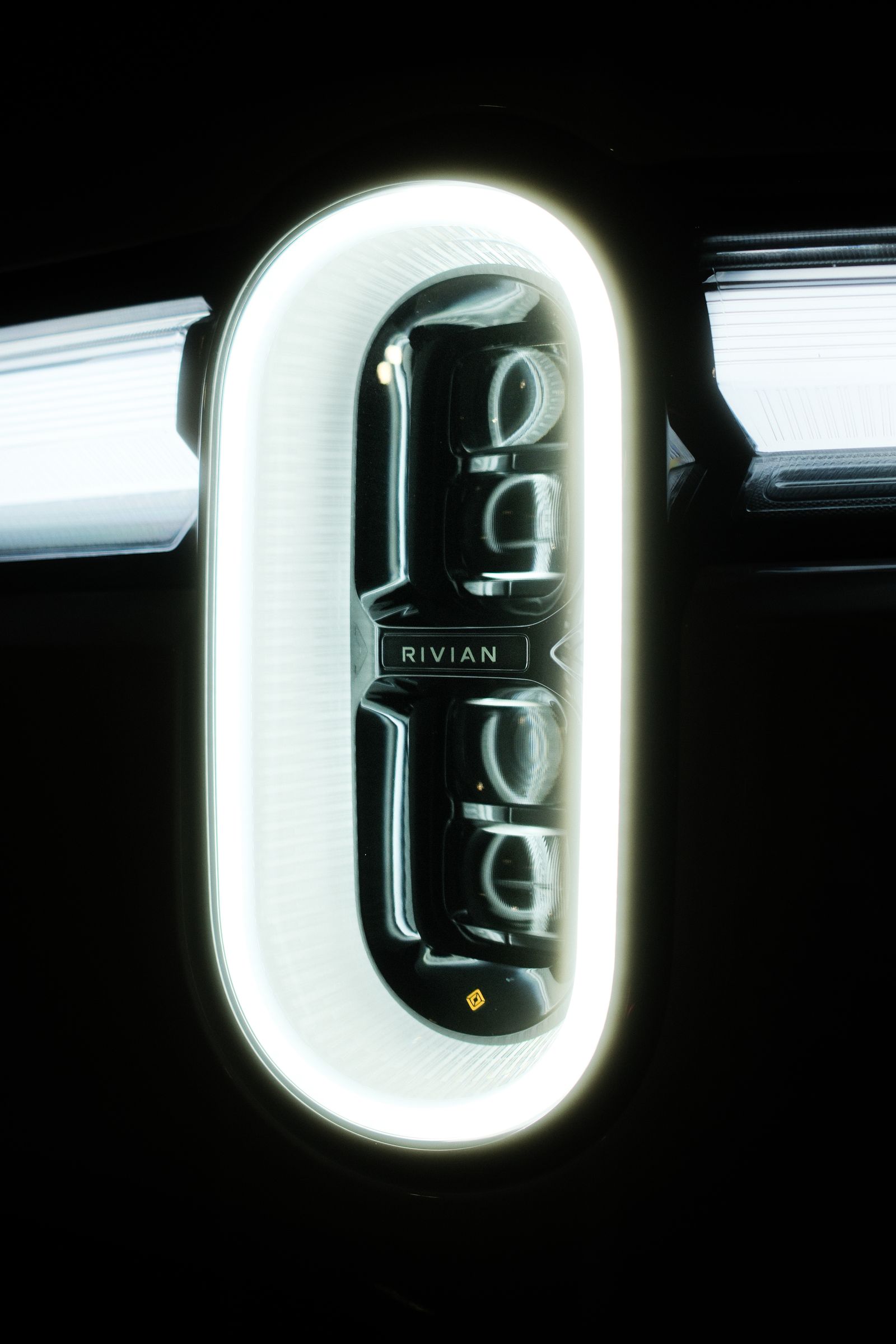 Close-up of a Rivian's glowing oval headlight in the dark
