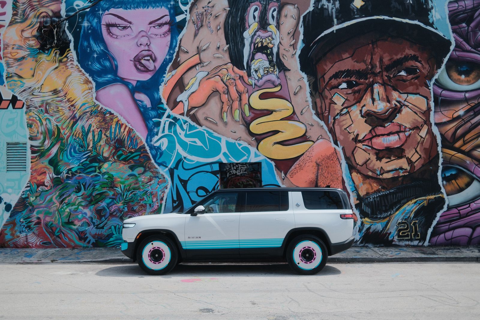 A white Rivian SUV parked in front of a huge colorful street mural