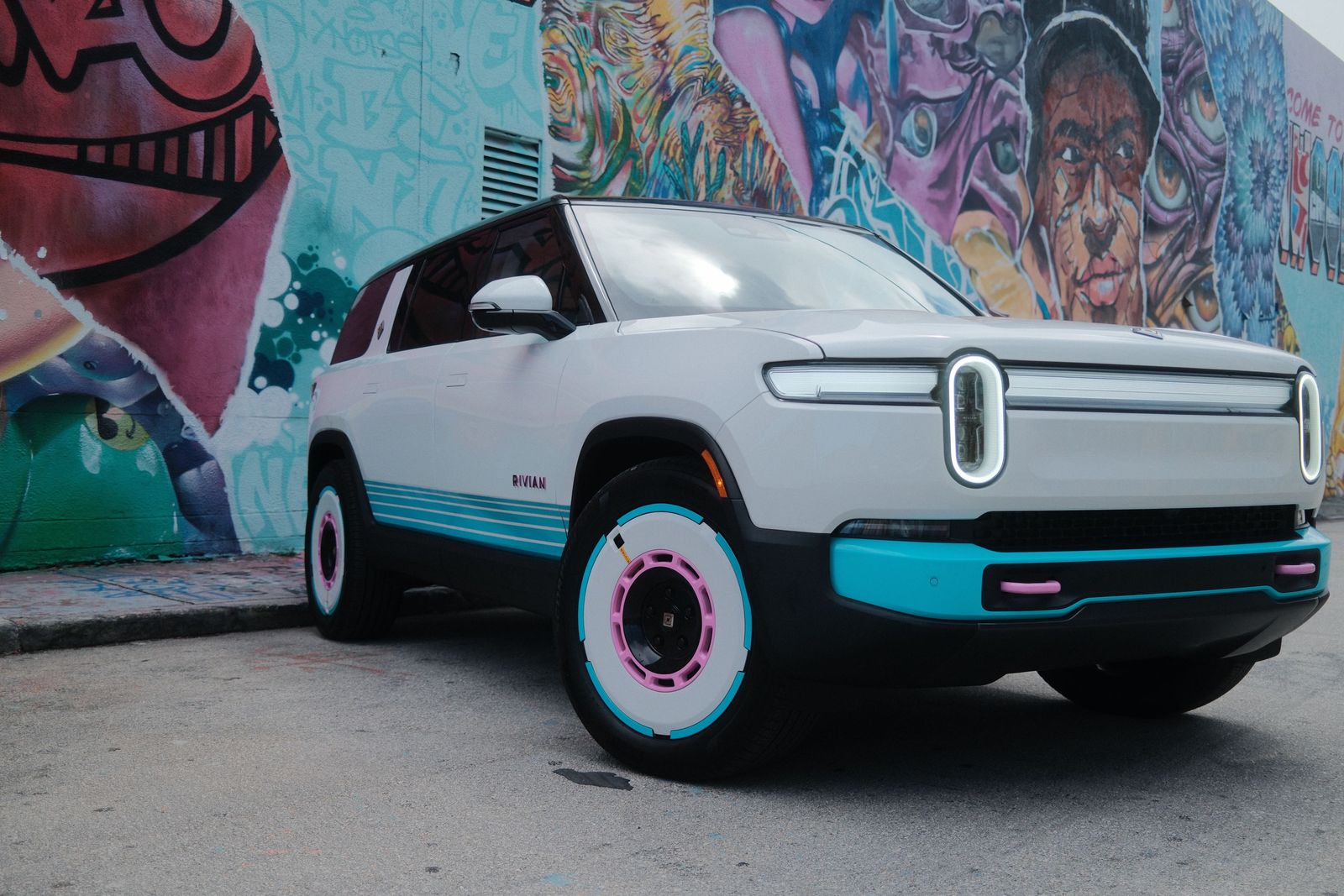 White Rivian R1S with teal and pink trim parked in front of a street mural