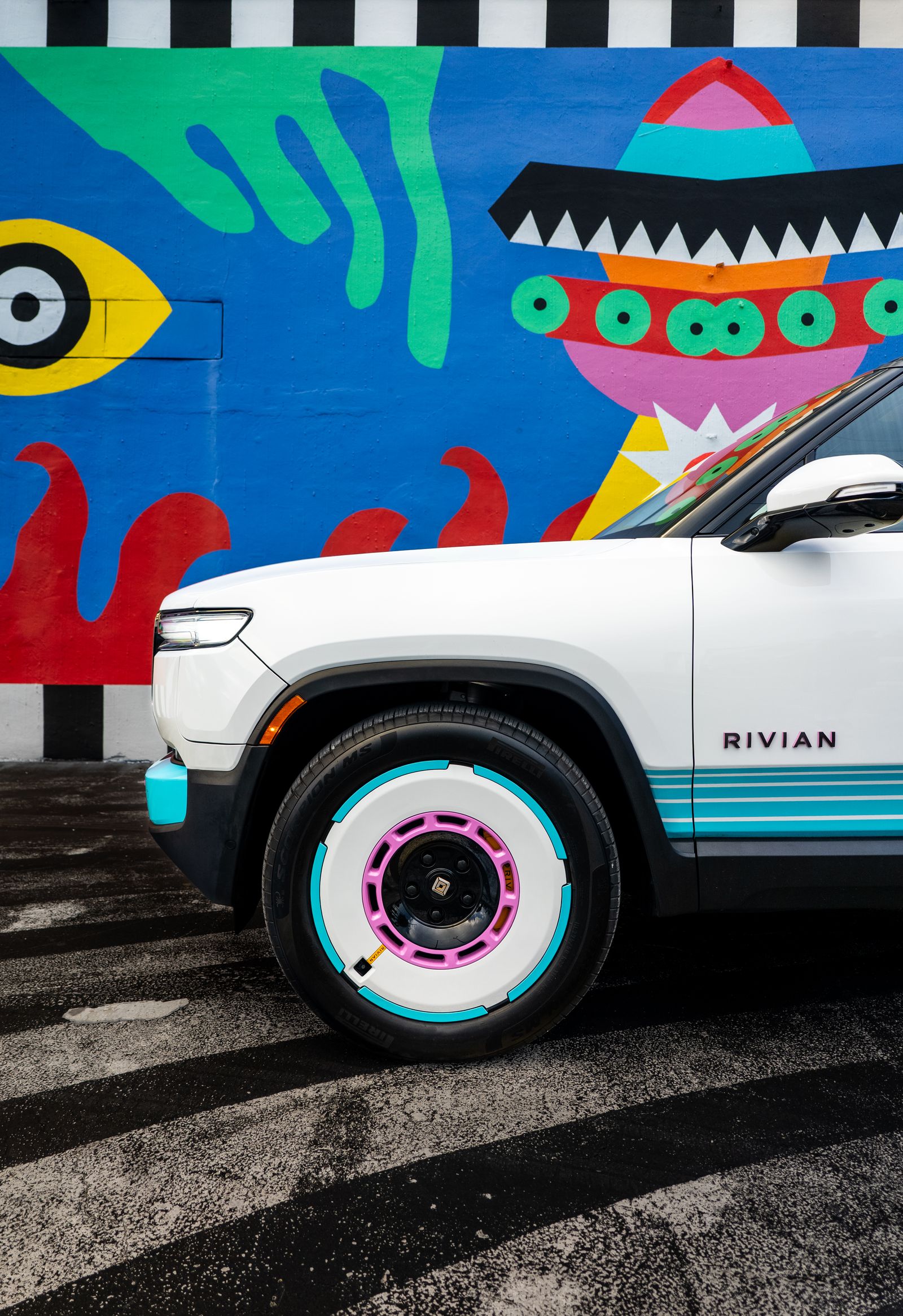 Close side view of a Rivian's front wheel against a bright graphic mural