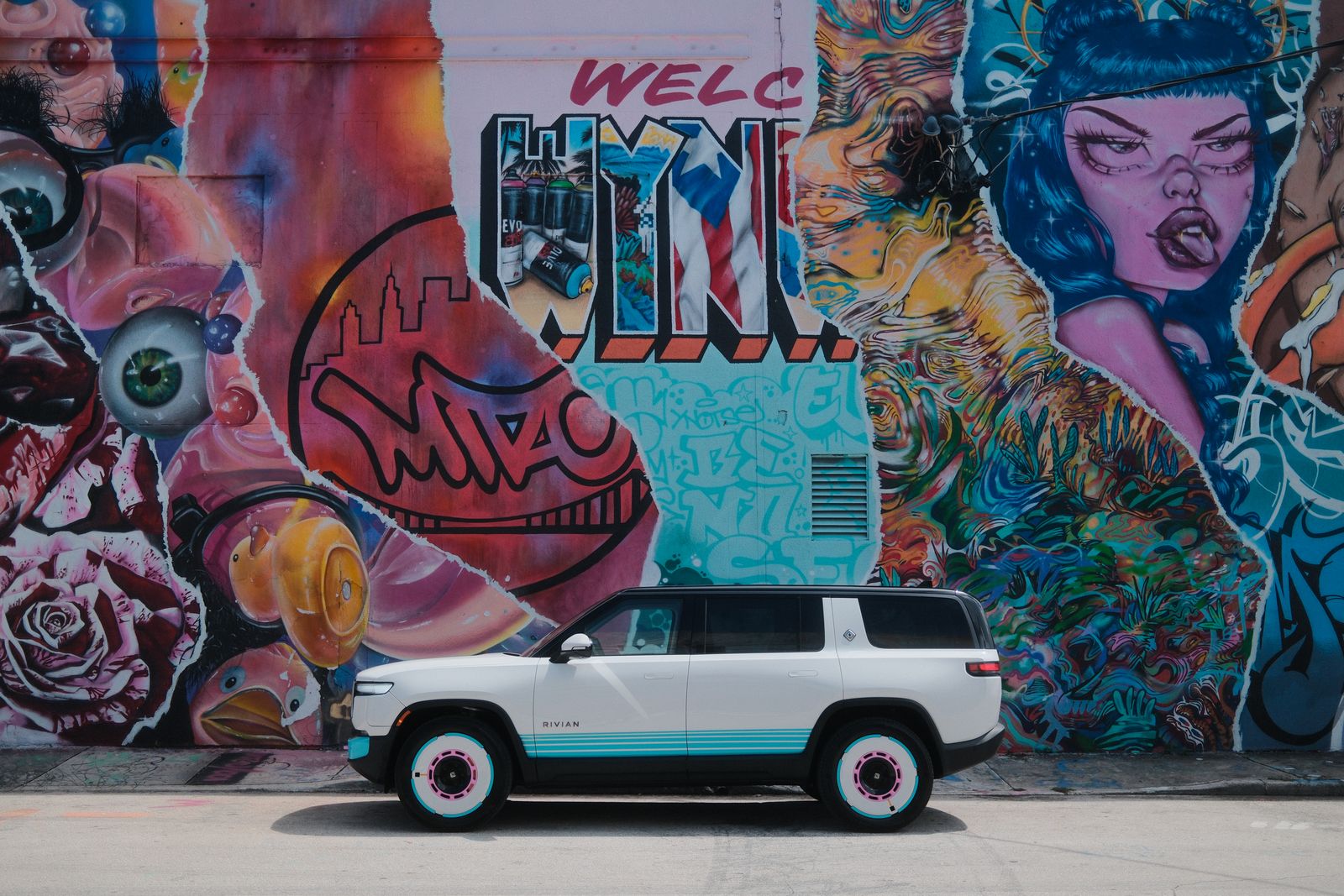 A white Rivian SUV in front of a packed Wynwood mural wall