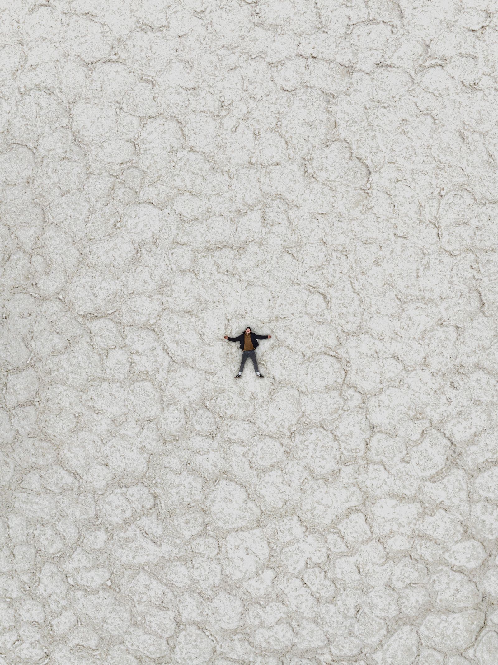 A person lying spread out on cracked white salt flats, seen from directly above