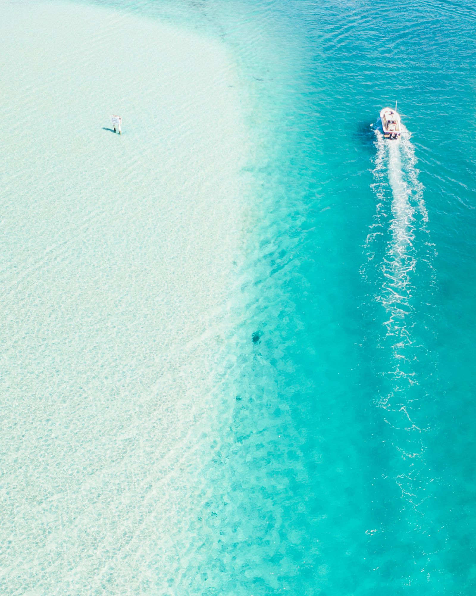 A boat carving a wake past a pale sandbar into deep turquoise water off Palm Beach