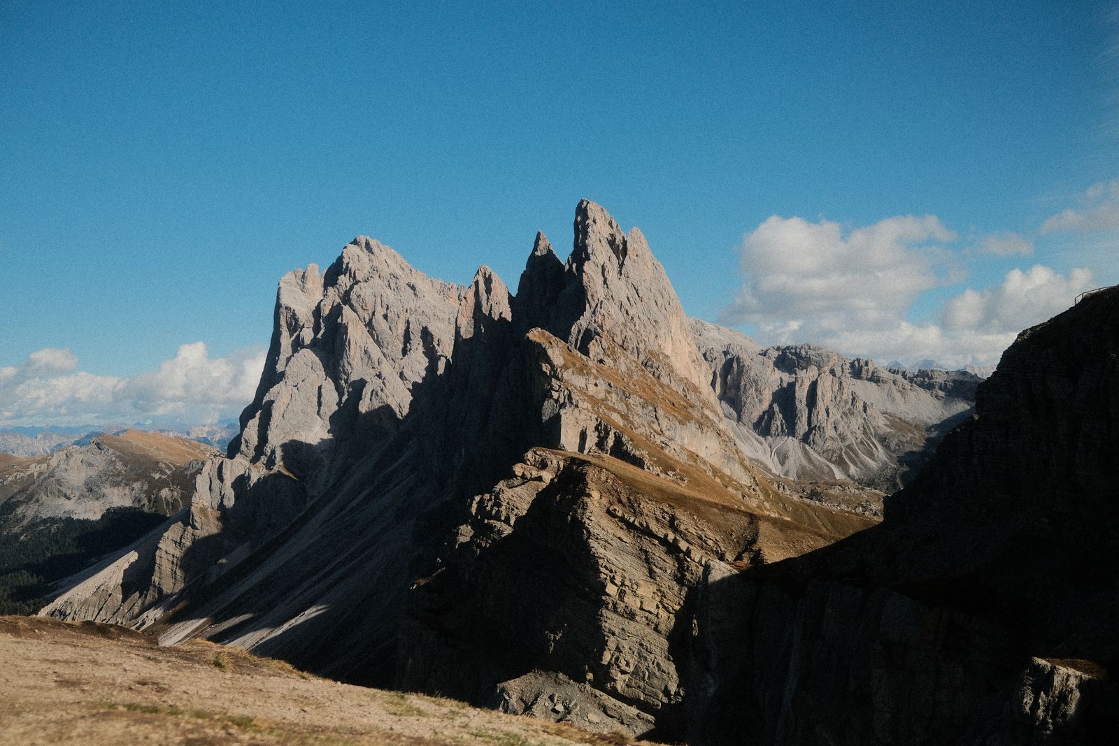 The jagged peaks of Seceda in the Dolomites under a blue sky with puffy clouds