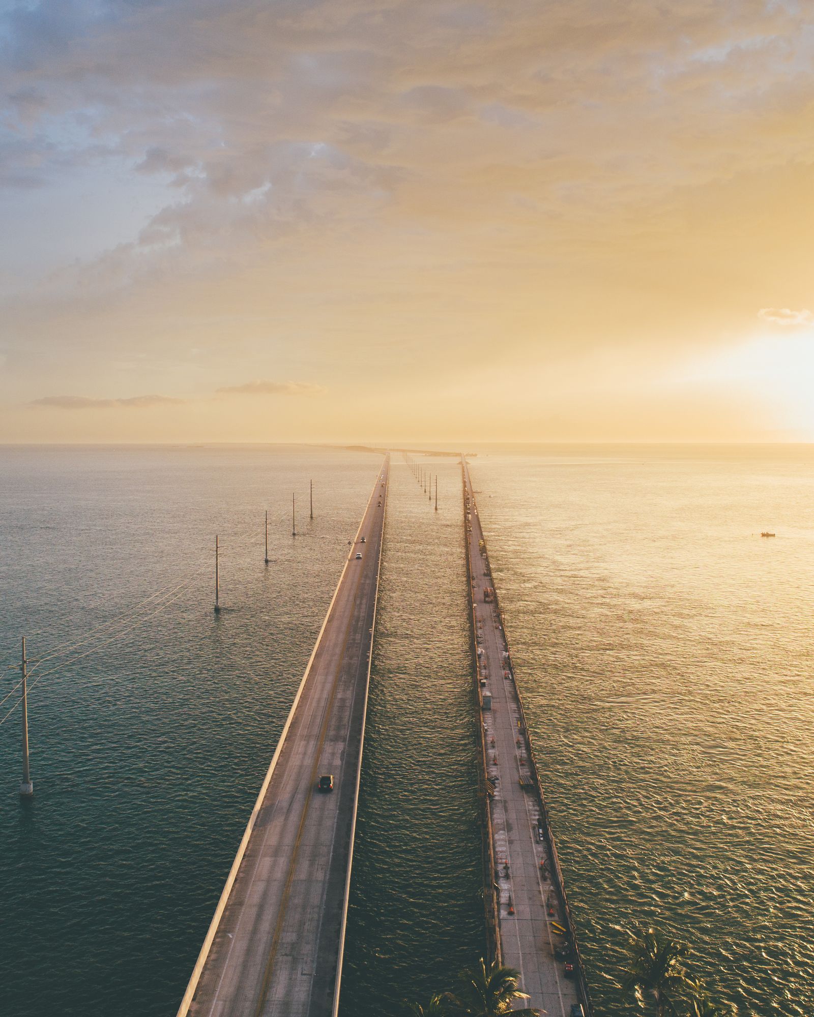 Aerial view down the Seven Mile Bridge in the Florida Keys at sunset, two spans running straight into a golden horizon