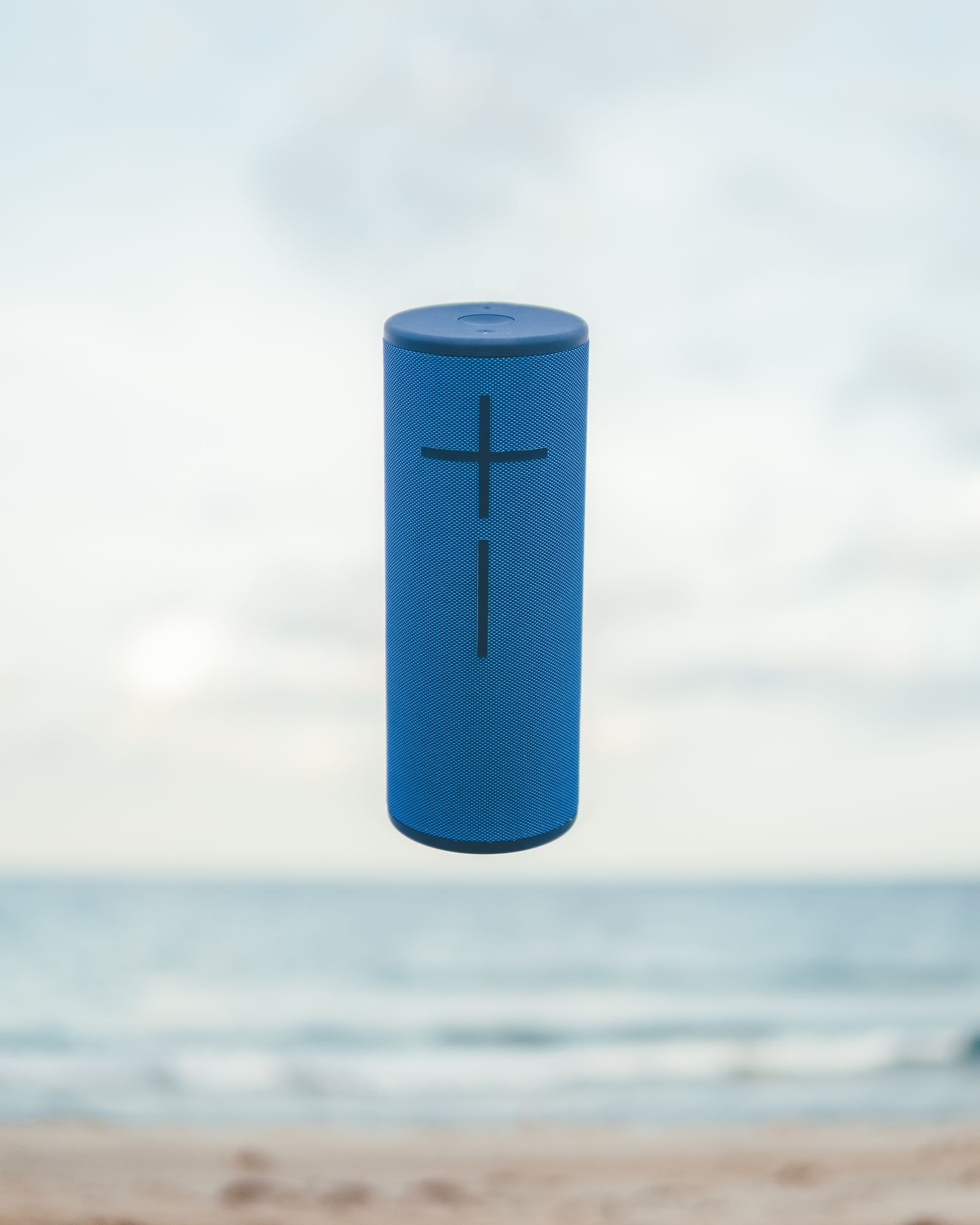 A blue Ultimate Ears MegaBoom speaker floating against a soft beach horizon